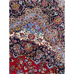 Persian Kashan crimson ground carpet, floral pattern indigo ground central medallion and matching spandrels, the field decorated densely with scrolling foliate patterns and floral motifs, the main border decorated with scrolling branches and palmettes, within floral pattern guard stripes