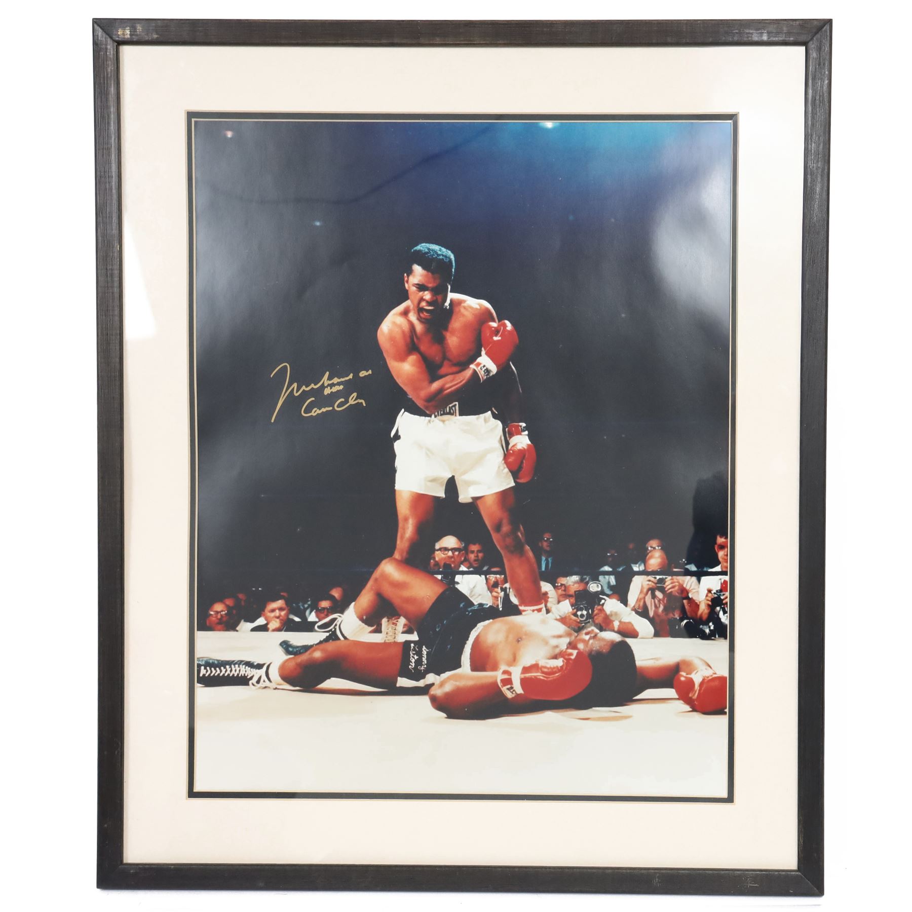 Large colour print depicting the famous scene of boxer Muhammad Ali standing over the defeated Sonny Liston, taken from their 1964 rematch, signed by Ali to the left middle in gold marker, with his double signature 'Muhammad Ali AKA Cassius Clay', with certificate of authenticity from Fraser's Autographs, framed, picture H49cm