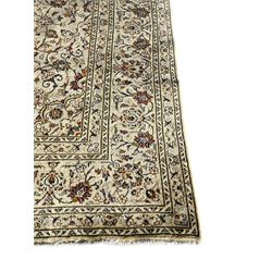 Persian Kashan ivory ground carpet, central medallion decorated with sixteen arranged palmette motifs, within a field decorated with swirling leafy branches and stylised plant motifs, the main border decorated with matching swirling pattern, within floral pattern guard stripes 