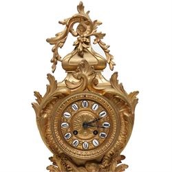 French-Late 19th century 8-day gilt brass rococo style mantel clock, c1890, waisted case  decorated with scroll work, leaves and musical instruments, resting on an attached plinth with splayed feet, dial within a glazed brass bezel with a gilt repoussé centre, porcelain cartouche Roman numerals and steel fleur-di-Lis hands, with a twin train movement, recoil anchor escapement and countwheel strike, sounding the hours and half-hours on a bell. With a matching pair of five-light candelabra. No Pendulum or Key.