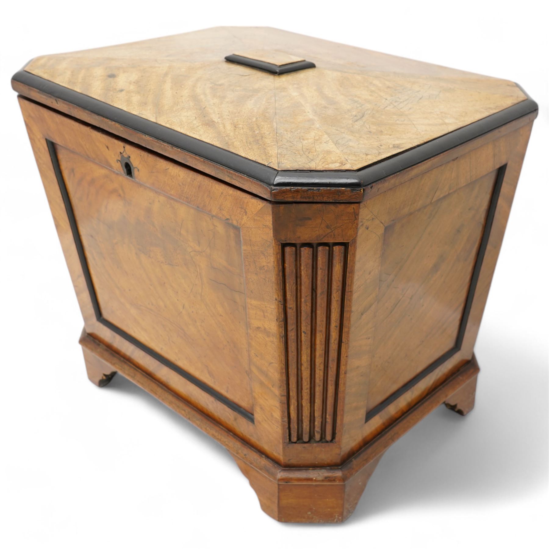 Early 19th century mahogany cellarette, tapering canted rectangular form, the hinged faceted top enclosing fitted interior, panelled front, back and sides with figured mahogany veneers, the canted corner with wide reeded decoration, on canted bracket feet 