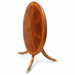 Regency design circular mahogany centre table, the radiating veneered top with contrasting crossbanded edge, on turned column support and four swept legs with brass paw feet and castors