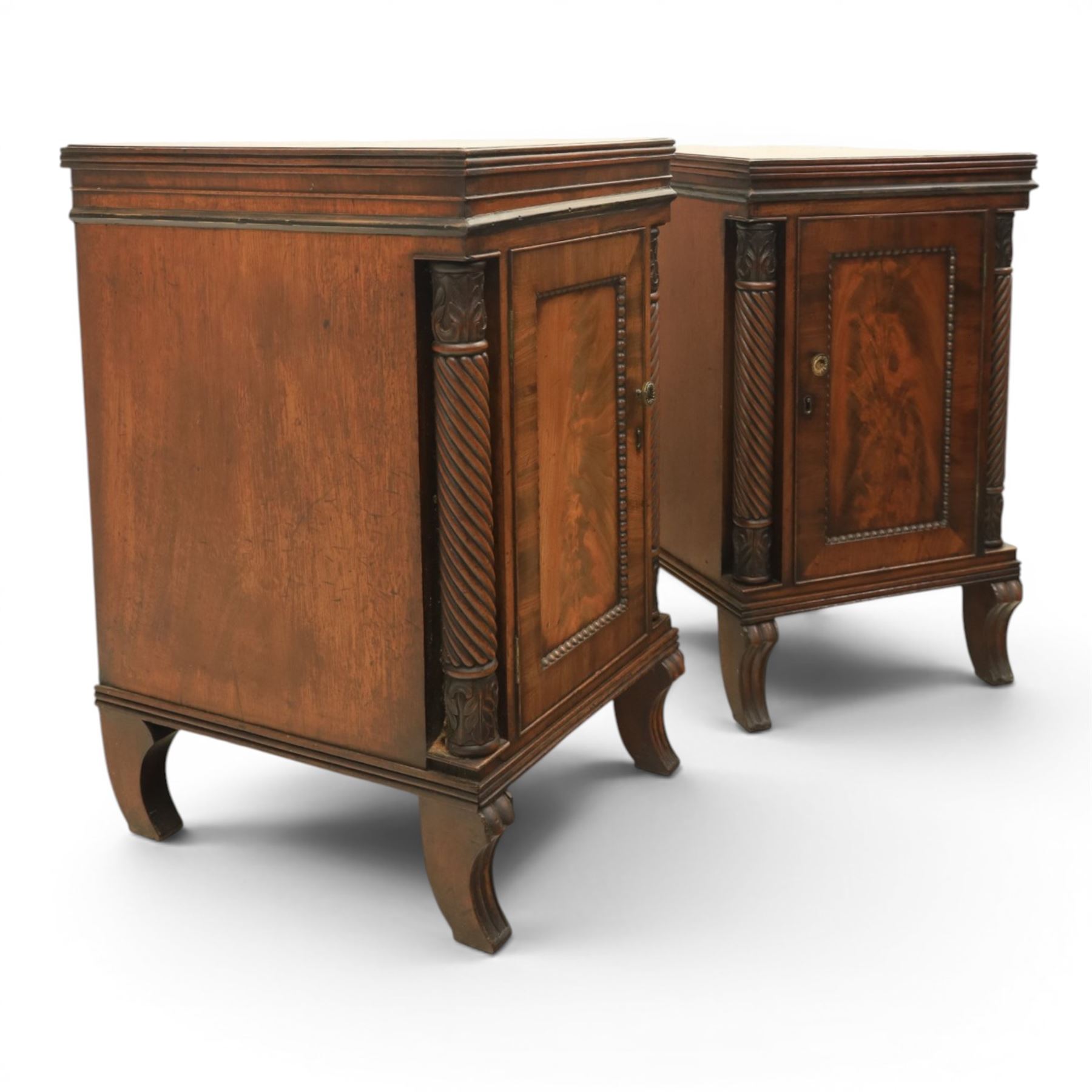  Pair of Regency mahogany bedside cabinets, rectangular top above a central cupboard door with flame mahogany veneer, flanked by spirally turned column uprights, raised on shaped supports