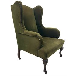 Early 20th century wingback armchair, wide seat, upholstered in green fabric with studded detail, cabriole front supports, on brass and ceramic castors 