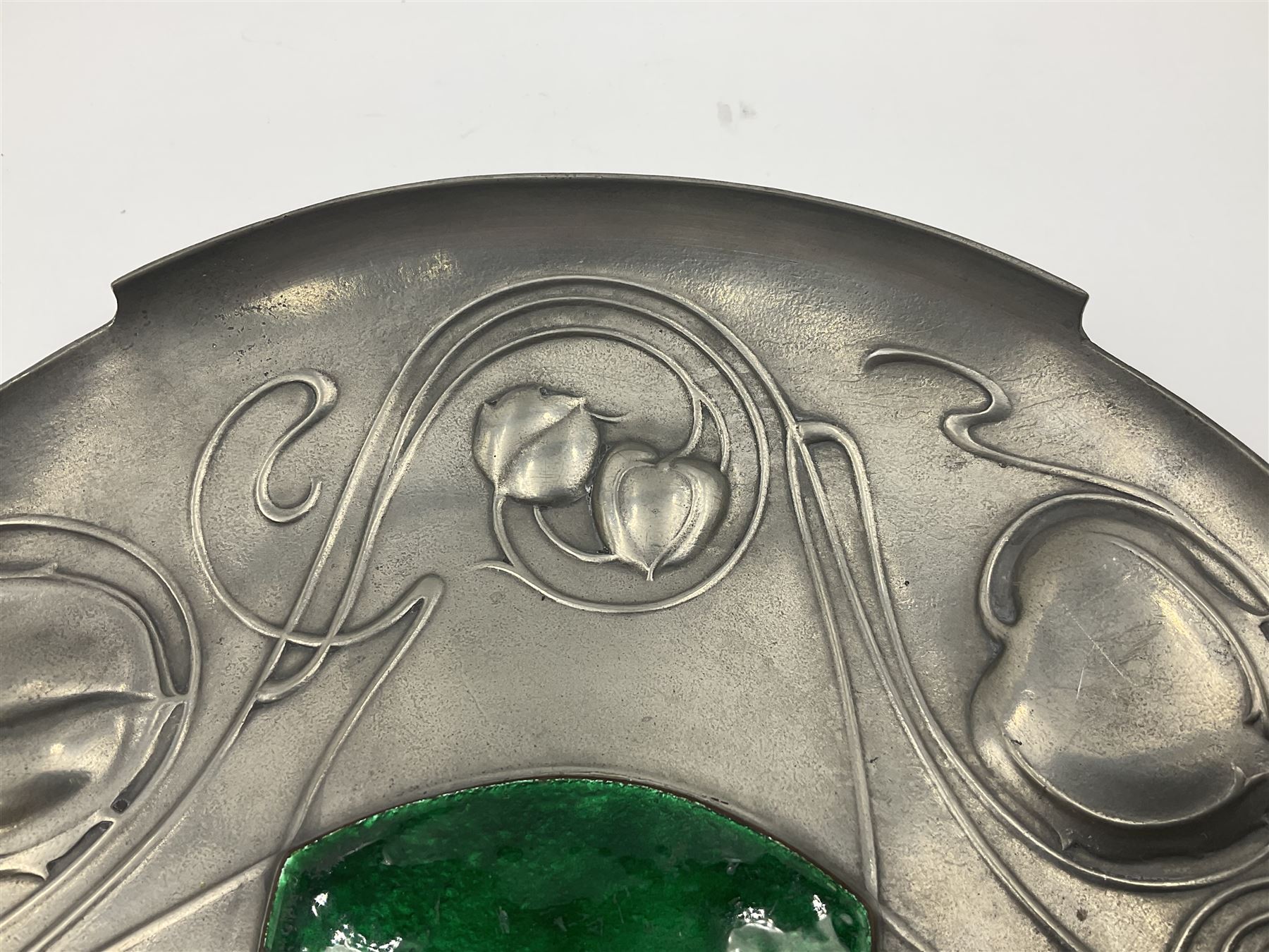 Liberty & Co Tudric pewter Bollelin tray, designed by Archibald Knox, of circular form with shaped edge, cast in relief with foliate tendrils surrounding a green enamel cartouche, impressed beneath Made by Library & Co English Pewter 044, D25.5cm