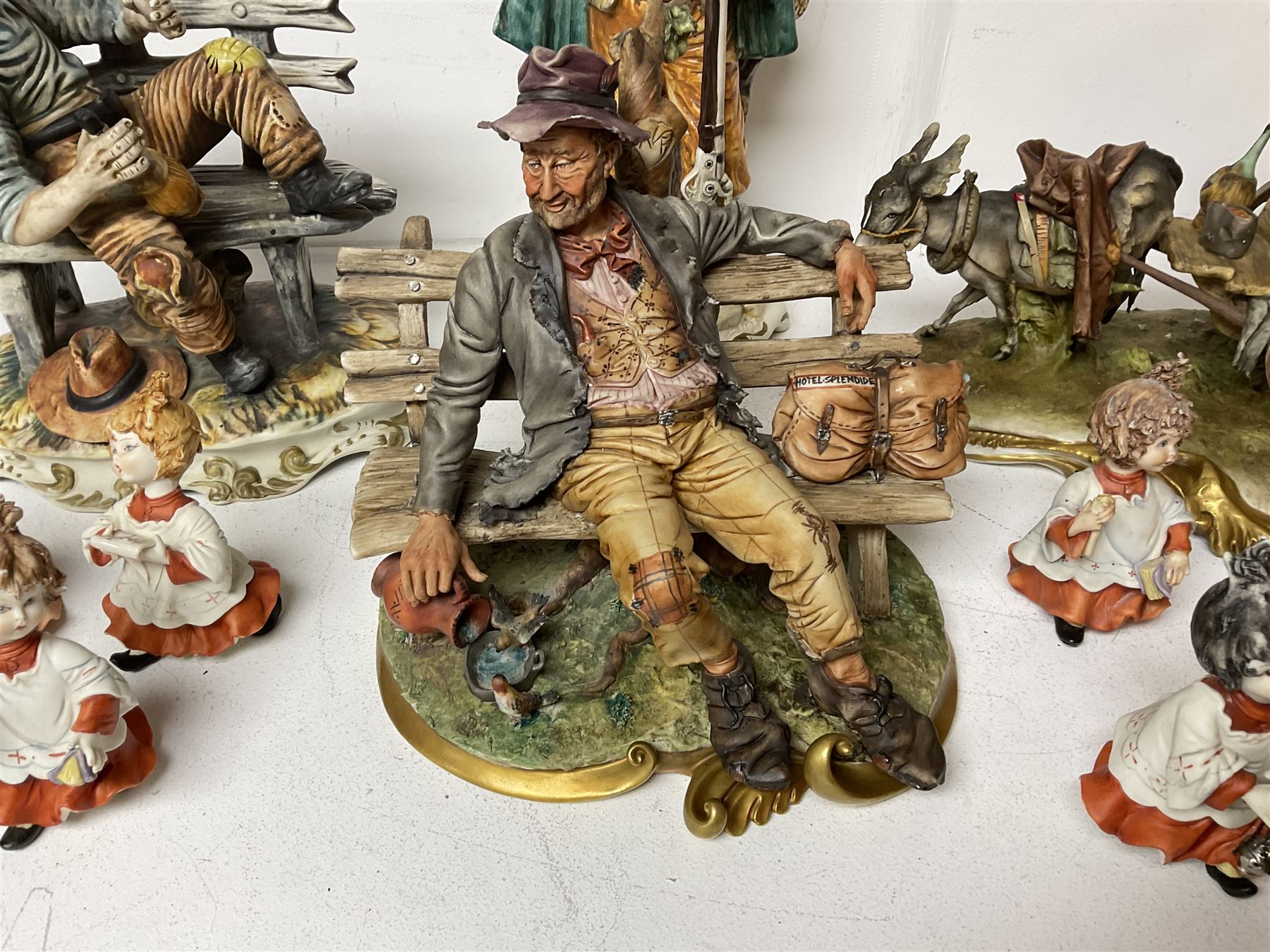 Group of Capodimonte figures, to include musical organ grinder with donkey and monkey, two tramp figures on benches, man with gun and choir boy and girl figures