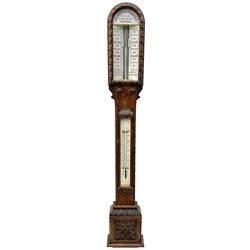 Negretti & Zambra of London - c1860 Victorian carved oak cistern tube storm barometer, with arch top glazed front ceramic scale inscribed “NEGRETTI & ZAMBRA OPTICIANS TO HER MAJESTY…LONDON” to panel above, double vernier canted scales inscribed with barometric air pressure in inches and weather predictions, rectangular trunk with vernier setting discs above a boxed Fahrenheit and Centigrade scale spirit thermometer, the base with carved cistern cover.  