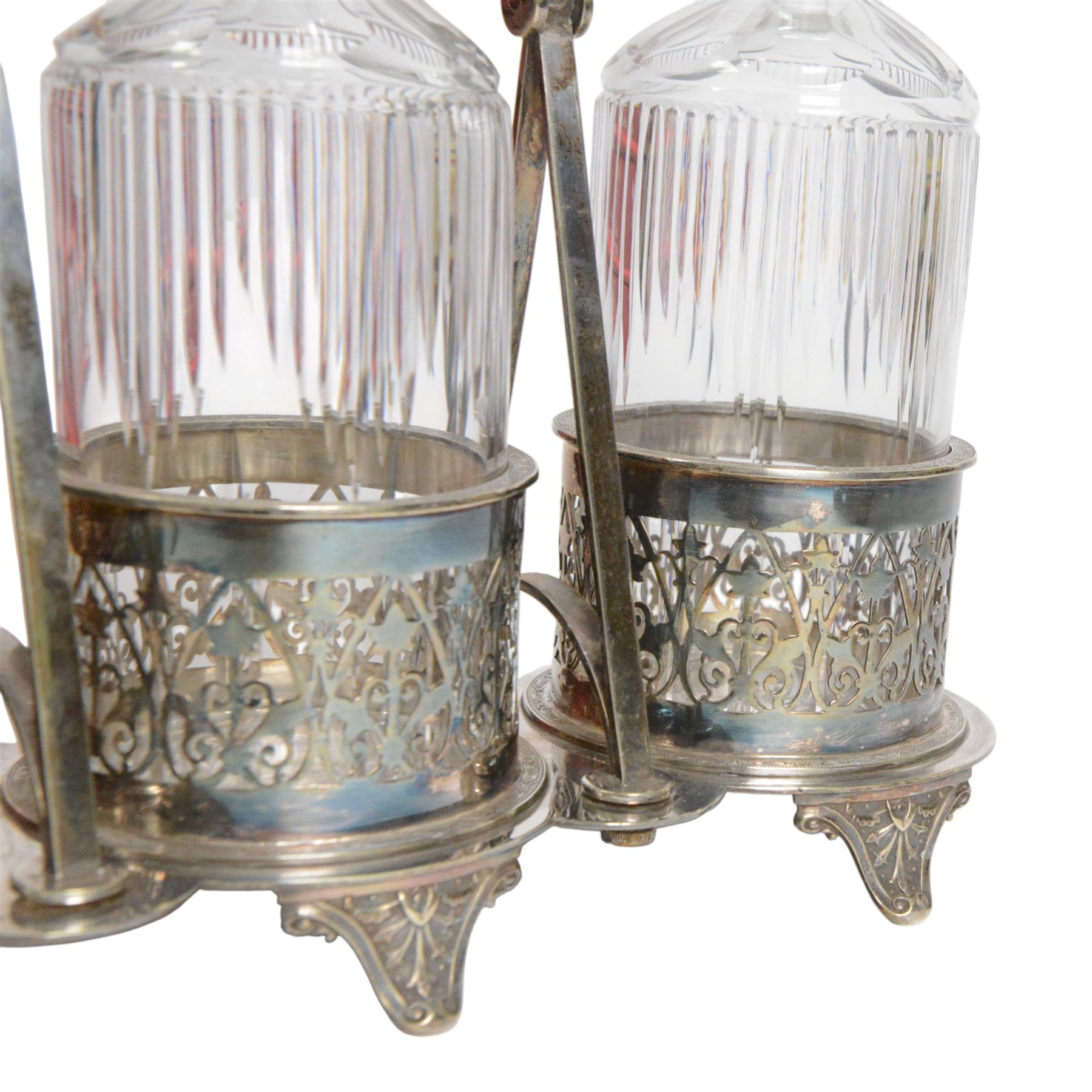 Late 19th century silver plated Silber & Fleming triple decanter stand, the three cut glass decanters with spire stoppers housed within foliate and scroll pierced bottle sleeves, upon a tripart base with six scroll feet, the base mounted with articulated x-frame curved handle, including handle when positioned upright H35.5cm, W34cm
