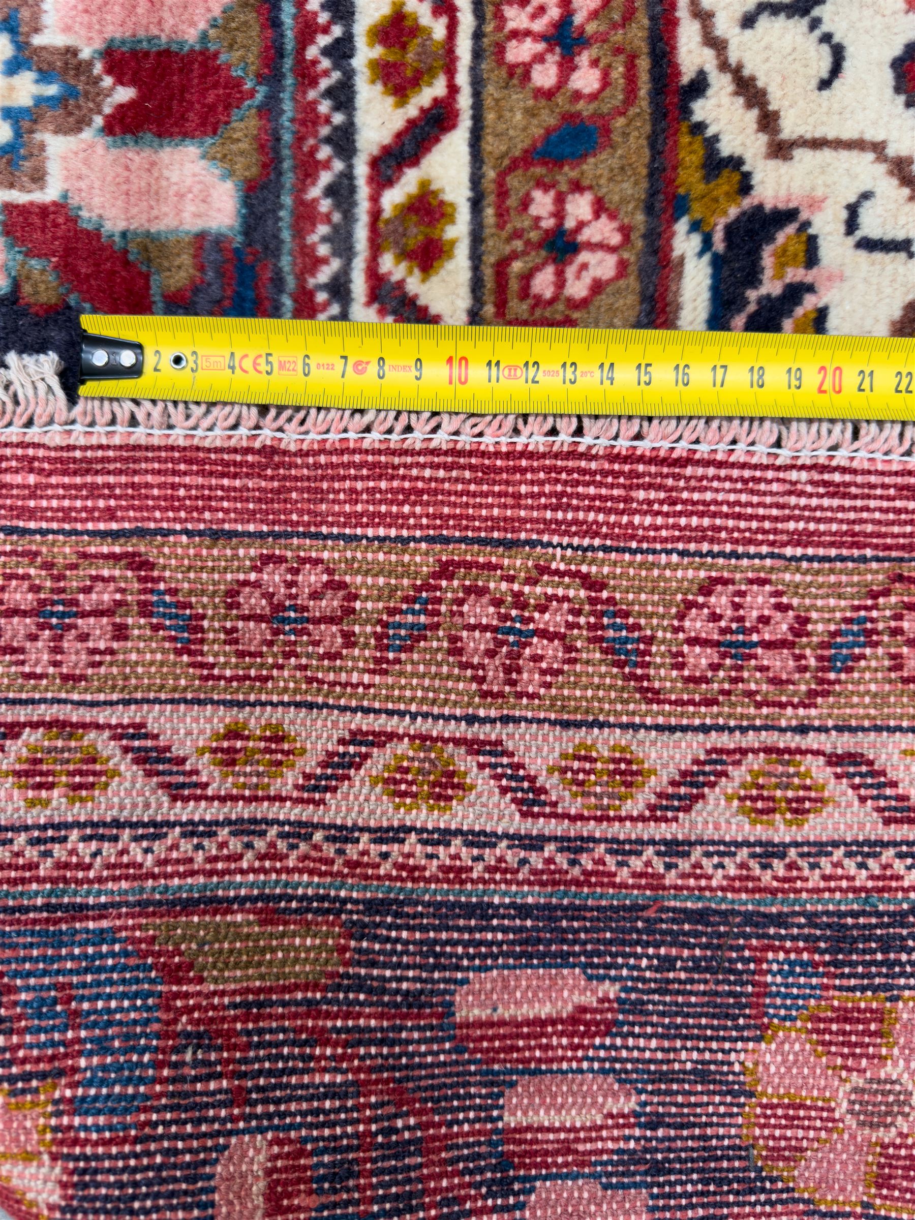 Northwestern Persian Lillihan hand-knotted carpet, madder red field with scrolling vines, rosettes, and palmettes around a central circular medallion in navy, ivory and ochre, and ivory ground spandrels within a navy border of stylized flowerheads and vines between multiple guard stripes 