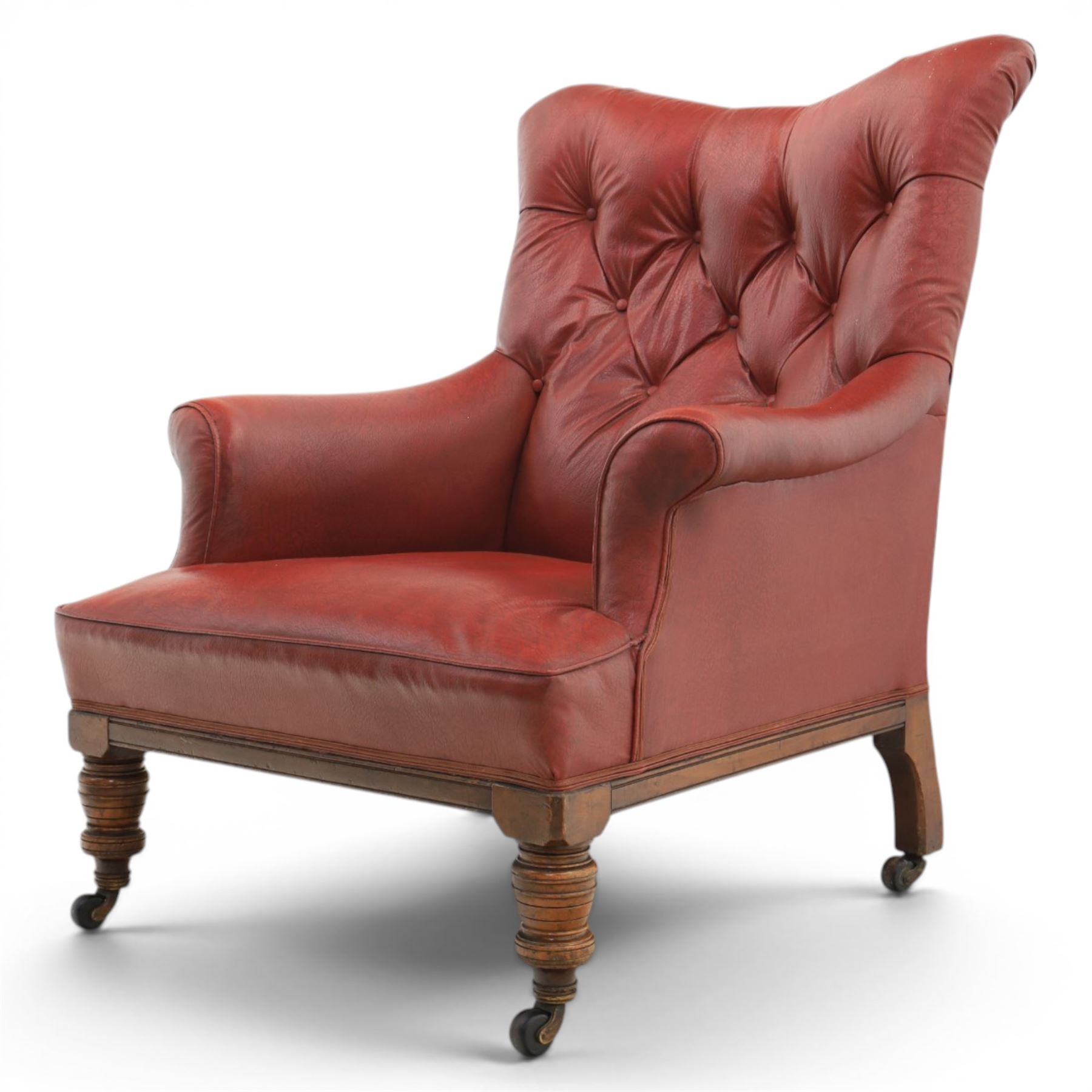 Early 20th century style oxblood red leather Chesterfield armchair, deep buttoned shaped back over padded scroll arms and loose seat cushion, raised on turned mahogany front supports with brass caps and castors