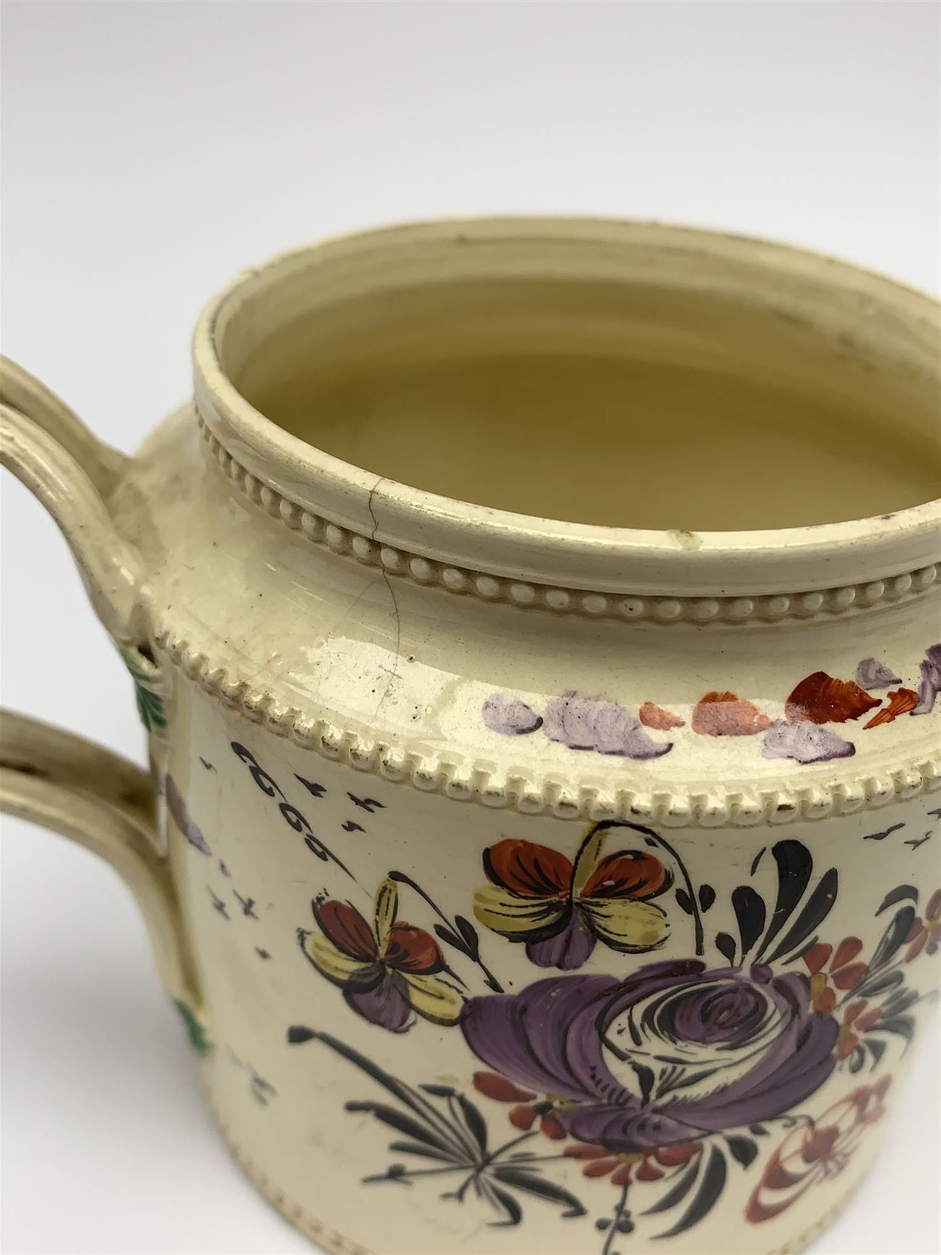 18th century creamware teapot, probably Leeds, with reeded entwined handle and floral finial to the cover, the body with hand painted polychrome decoration of figure to one side, and floral spray to the other, collectors paper label beneath inscribed Leeds Pottery, H11.5cm