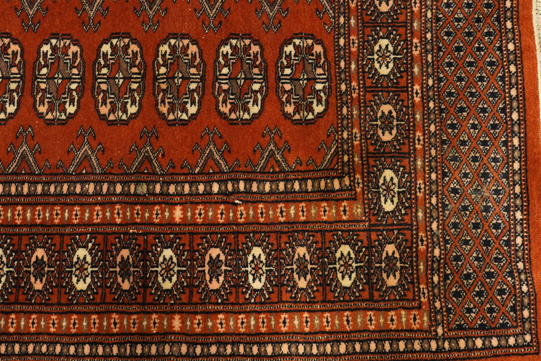 Bokhara hand-knotted carpet, terracotta ground with repeating rows of Tekke guls interspersed with geometric motifs, enclosed by multiple stylised floral and geometric borders, with fringed ends