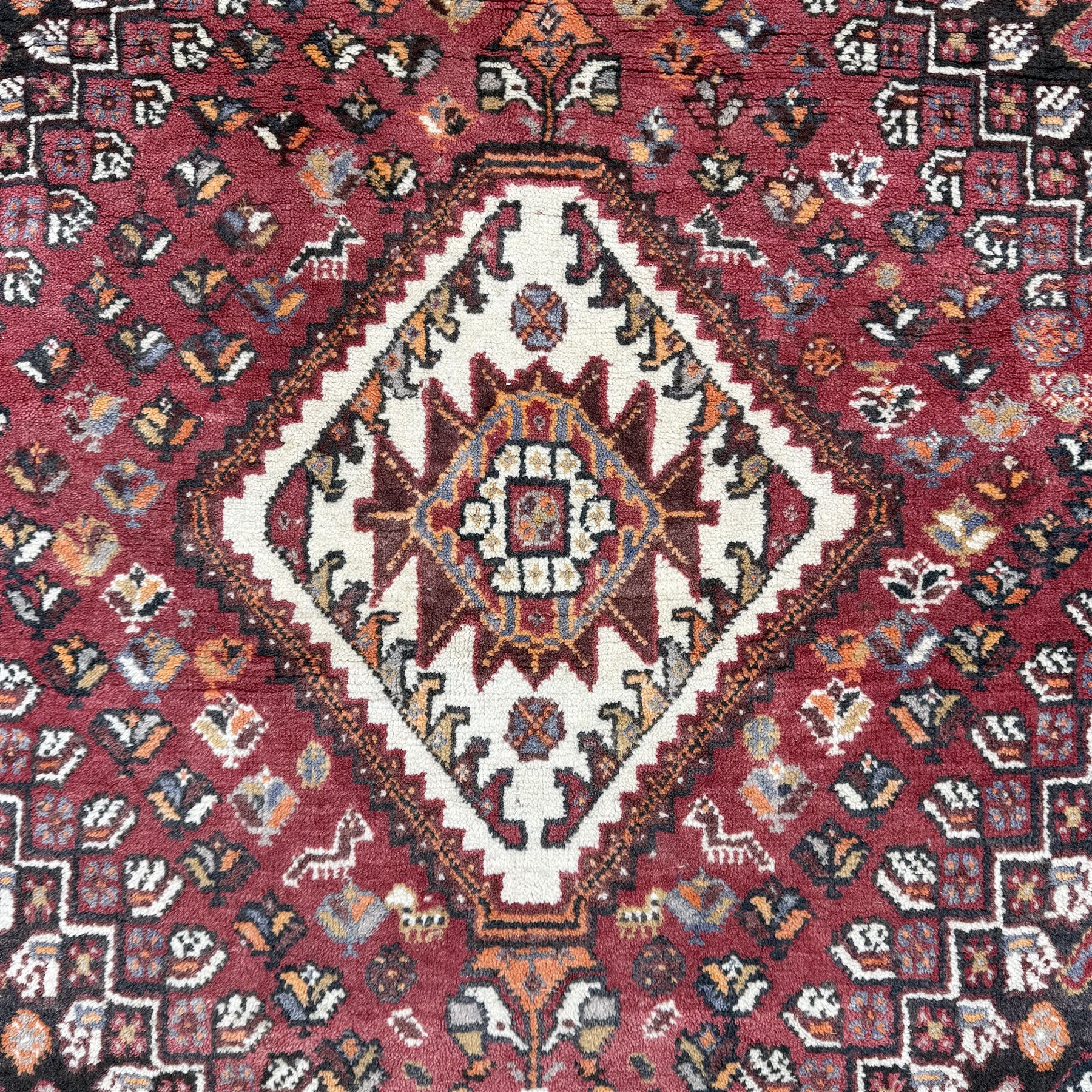 Southwestern Persian Qashqai rug, central diamond medallion with hooked motifs flanked by four corner medallions on a rich red madder field with dark brown ground of stylized floral and animal motifs, and ivory border with alternating floral palmettes and a red main  border with a meandering vine pattern 