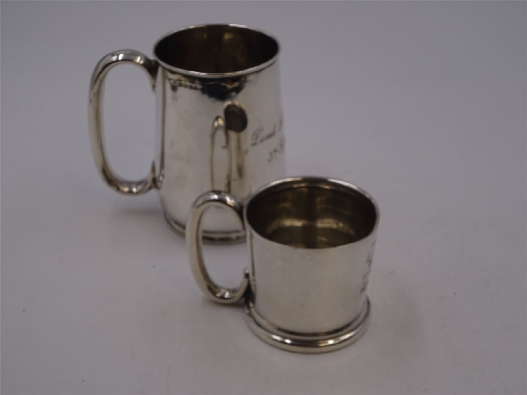 Early 20th century silver christening mug, of tapering cylindrical form, with C handle and personal engraving to centre, upon stepped base, hallmarked Chester 1913, maker's mark worn and indistinct, together with a Victorian silver christening mug, of slightly tapering form, with C handle, later personal engraving to centre and beaded rim to base, hallmarked James Dixon & Sons Ltd, Sheffield 1880, tallest H9cm