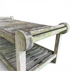 Lutyens design weathered teak garden bench with matching two-tier table, the bench with shaped arched and slatted back over rolled arms and slatted seat