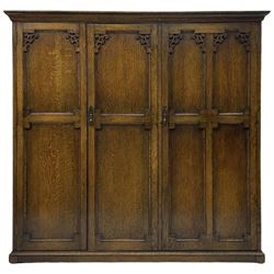 Early 20th century oak triple wardrobe, three panelled doors with geometric mouldings and fretwork spandrels, the interior fitted with slides and hanging rail