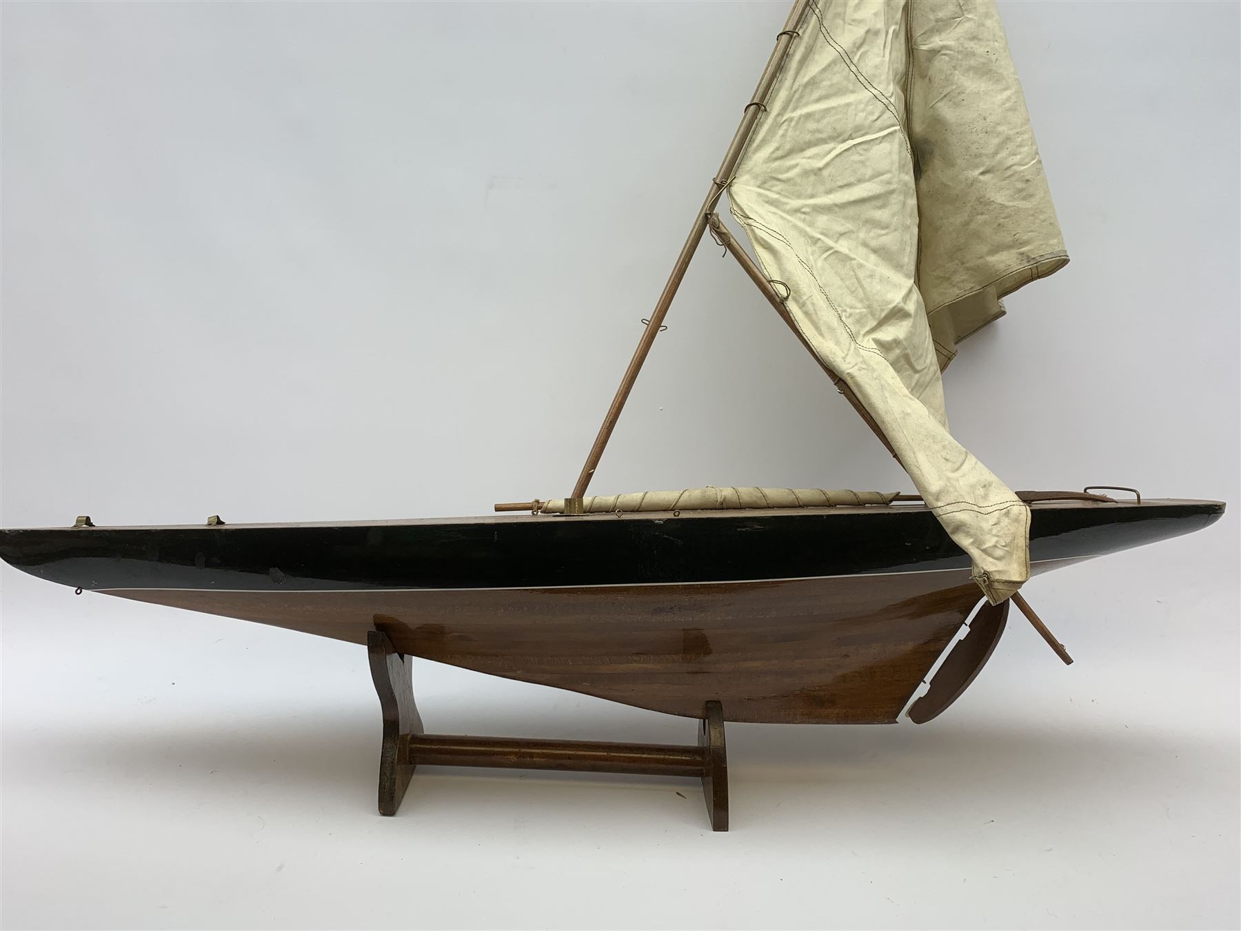 Pond yacht with part black painted mahogany hull and keel, working rudder and mast with three sails W90cm H95cm, loose mounted on mahogany stand