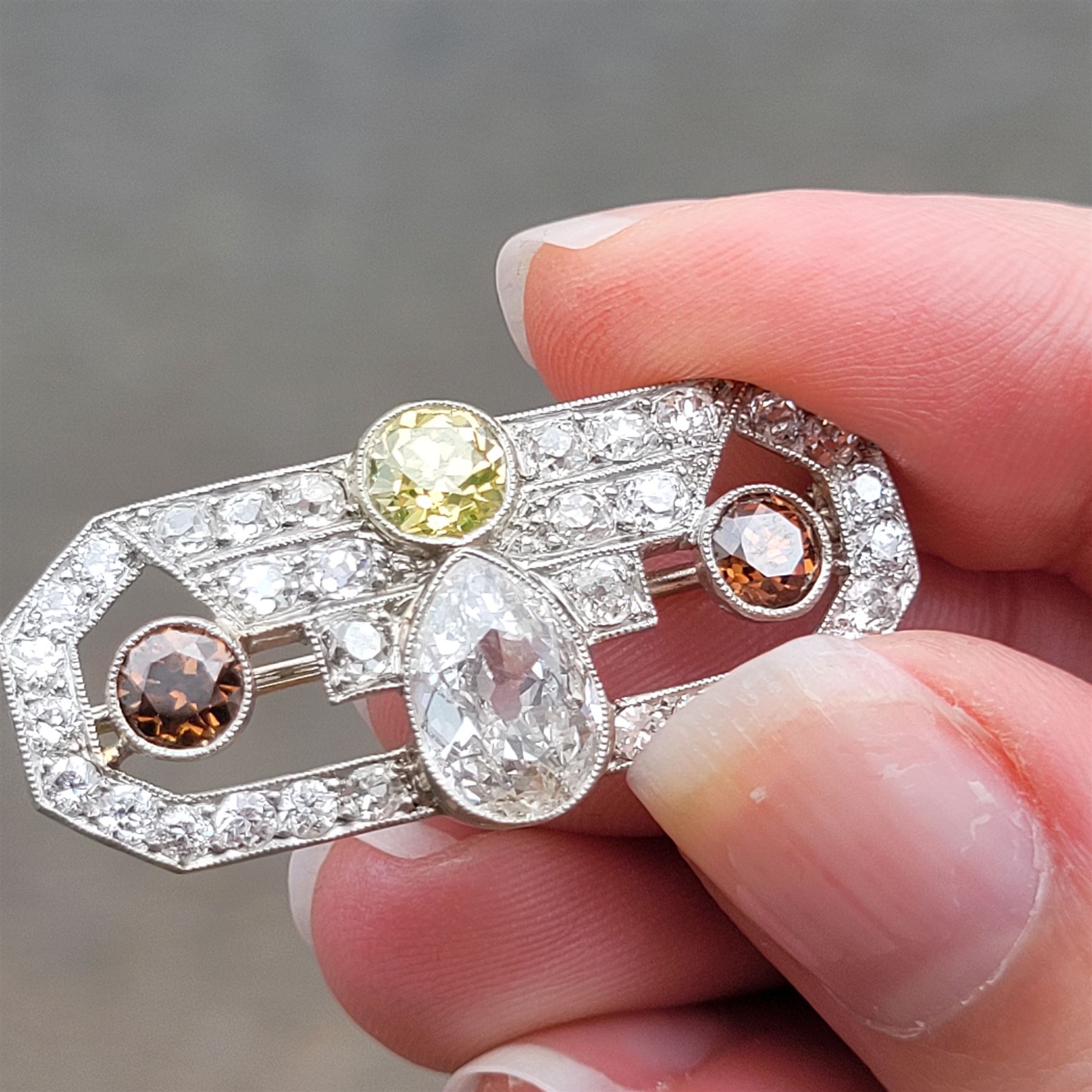 Early 20th century platinum diamond brooch, milgrain set with a pear cut faint brown diamond of approx 1.50 carat, an old cut fancy yellow / green diamond of approx 0.70 carat, and two old cut fancy orange / brown diamonds of approx 0.40 carat and 0.35 carat, surrounded by old cut white diamonds in an openwork setting, total white diamond weight approx 1.45 carat