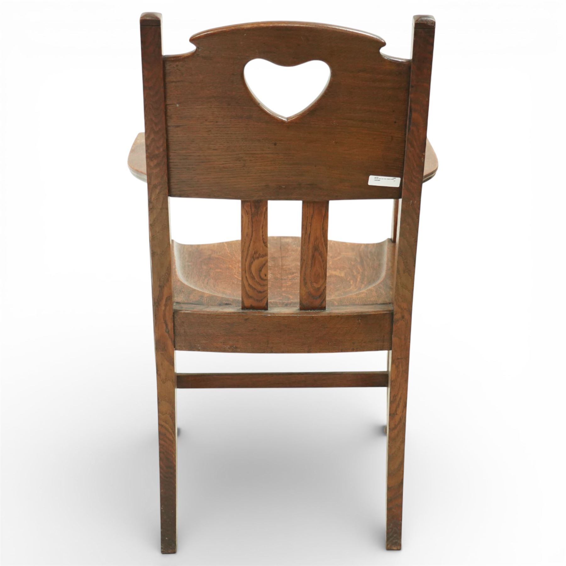 Arts and Crafts oak armchair, the shaped back with heart-shaped pierced splat above three vertical slats, solid dished seat with rounded front, open arms on turned front supports, square section legs united by plain stretchers
