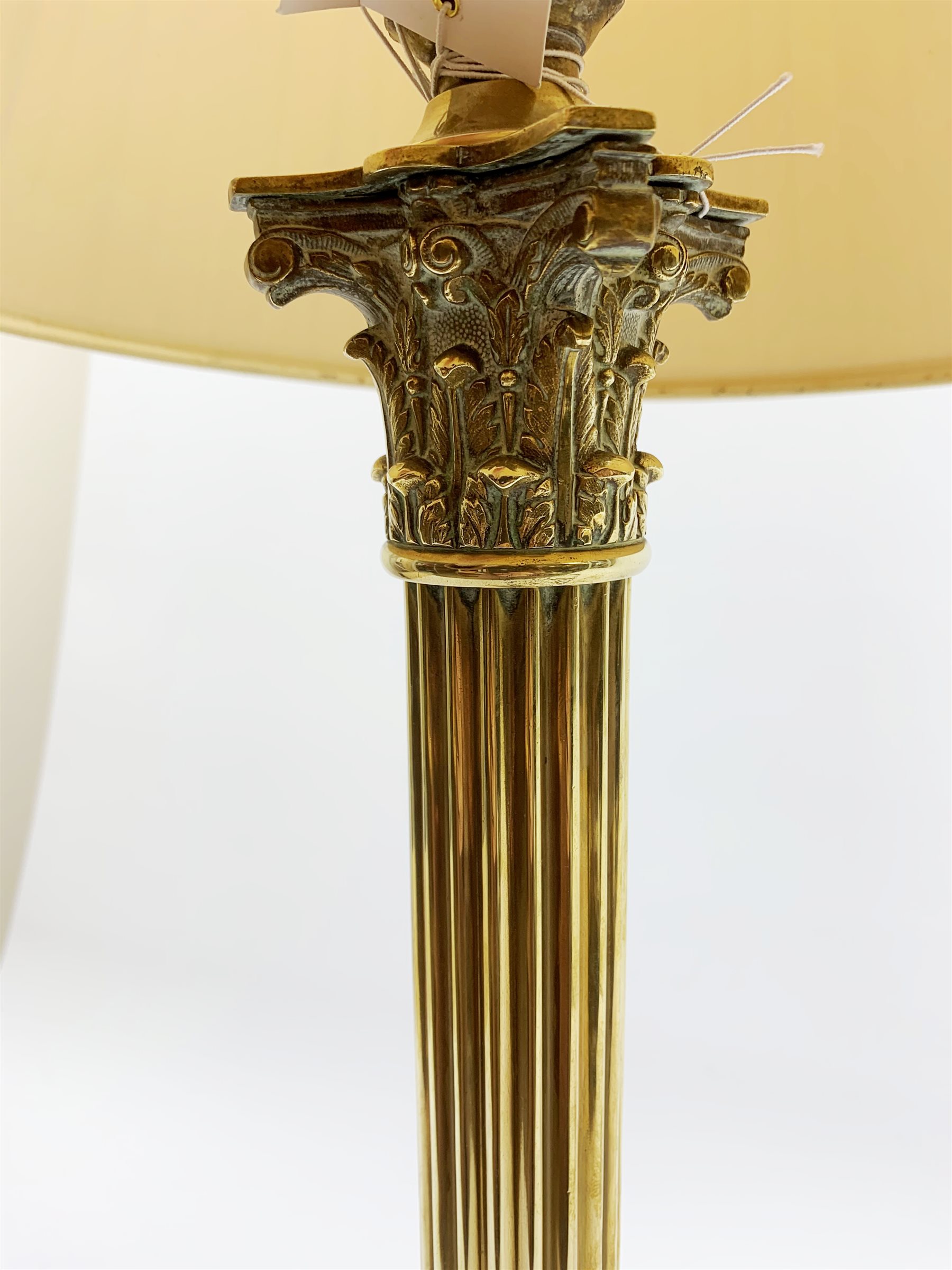 A brass Corinthian column table lamp, on stepped square base, including fitting H57cm, with pleated shade.