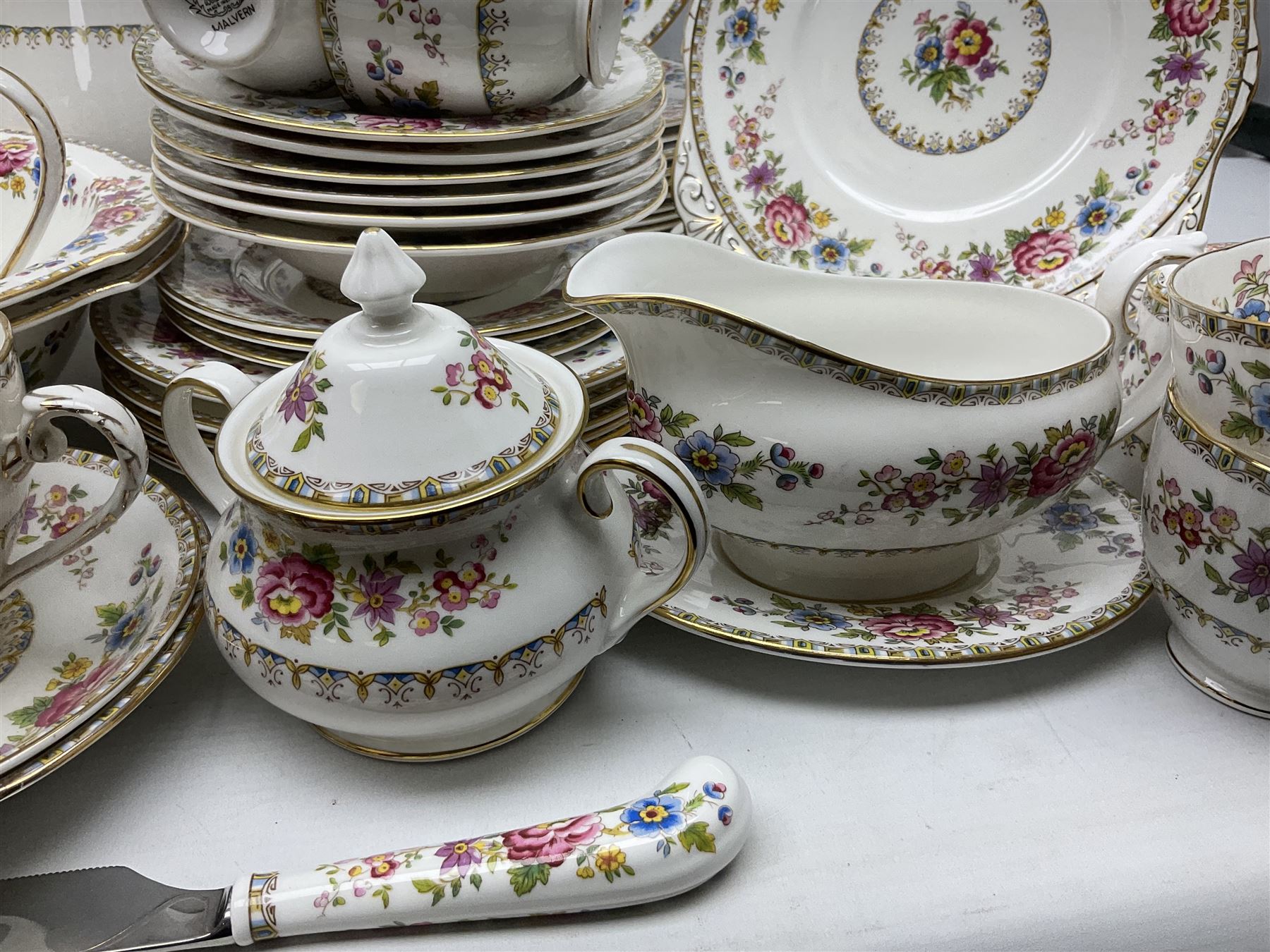 Extensive Royal Grafton Malvern pattern tea and dinner wares, comprising twelve dinner plates, six smaller plates, coffee pot, two teapots, two cake plates, eight teacups and ten saucers, six coffee cups and six saucers, two open sucriers, twin handled lidded sucrier, jug, lidded mustard pot and condiment jar, lidded tureen, two circular twin handled vegetable tureens, sauce boat and stand, oval and circular serving plates, salt and pepper shakers, breakfast cup and two saucers, further large cup and saucer, eighteen tea plates of various shapes, six side plates, six cereal bowls and six further bowls, shell dish and dish of square form, fork and knife, together with a hallmarked silver condiment spoon