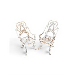 Pair of Victorian cast iron garden chairs, the ornate pierced back of scrolling foliate design, scrolling arm terminals over splayed supports formed of C and S-scrolls, in distressed white painted finish