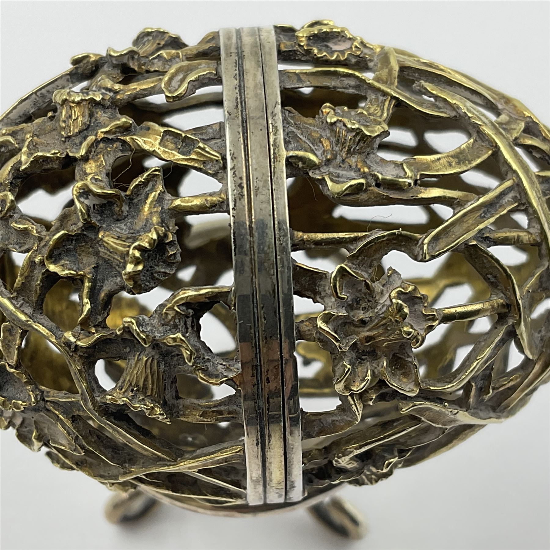Modern silver limited edition Easter egg, no. 70/500, the gilt openwork body decorated with daffodils and detachable cover with pierced circular panel set with a single faceted blue stone, opening to reveal a gilt interior, upon silver stand with three scrolling pad feet, each hallmarked St James House Company, London 1980, height including stand 8cm
