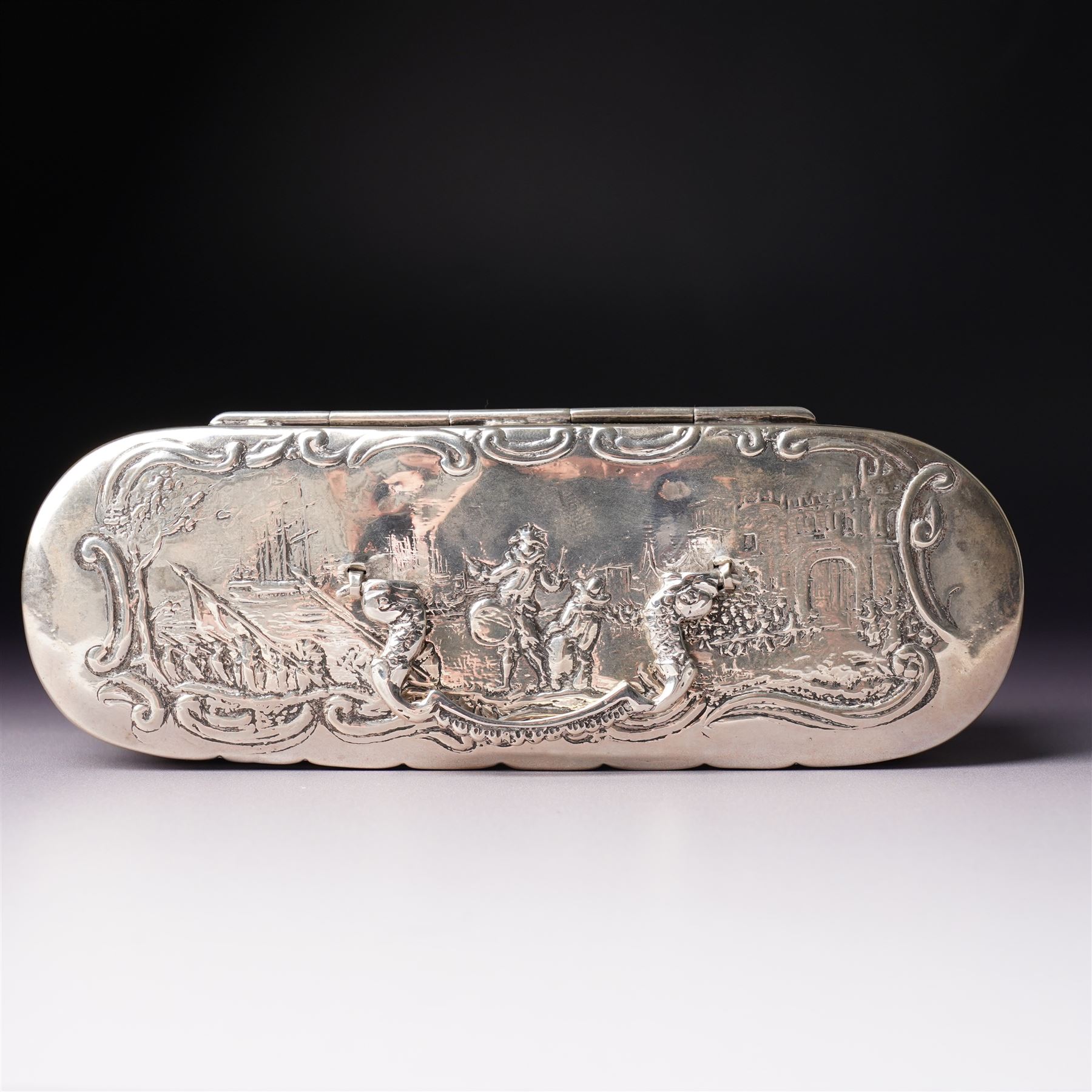 19th century continental silver box of oval design , the hinged cover with swing handle embossed with sailing ships, castle etc, the base decorated with horse and cart in rural landscape and the sides with a hunting scene on ball feet L15cm
