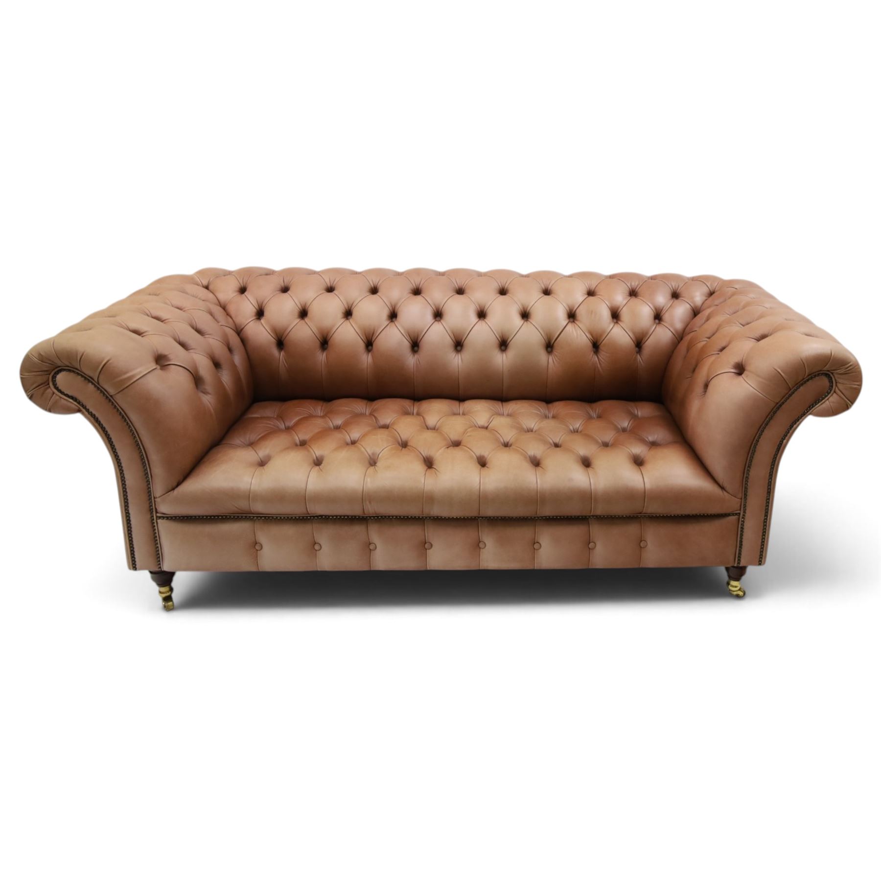 Distinctive Chesterfield - full buttoned tan brown leather sofa, deep buttoned back, seat and arms, raised on dark stained supports terminating in brass castors 