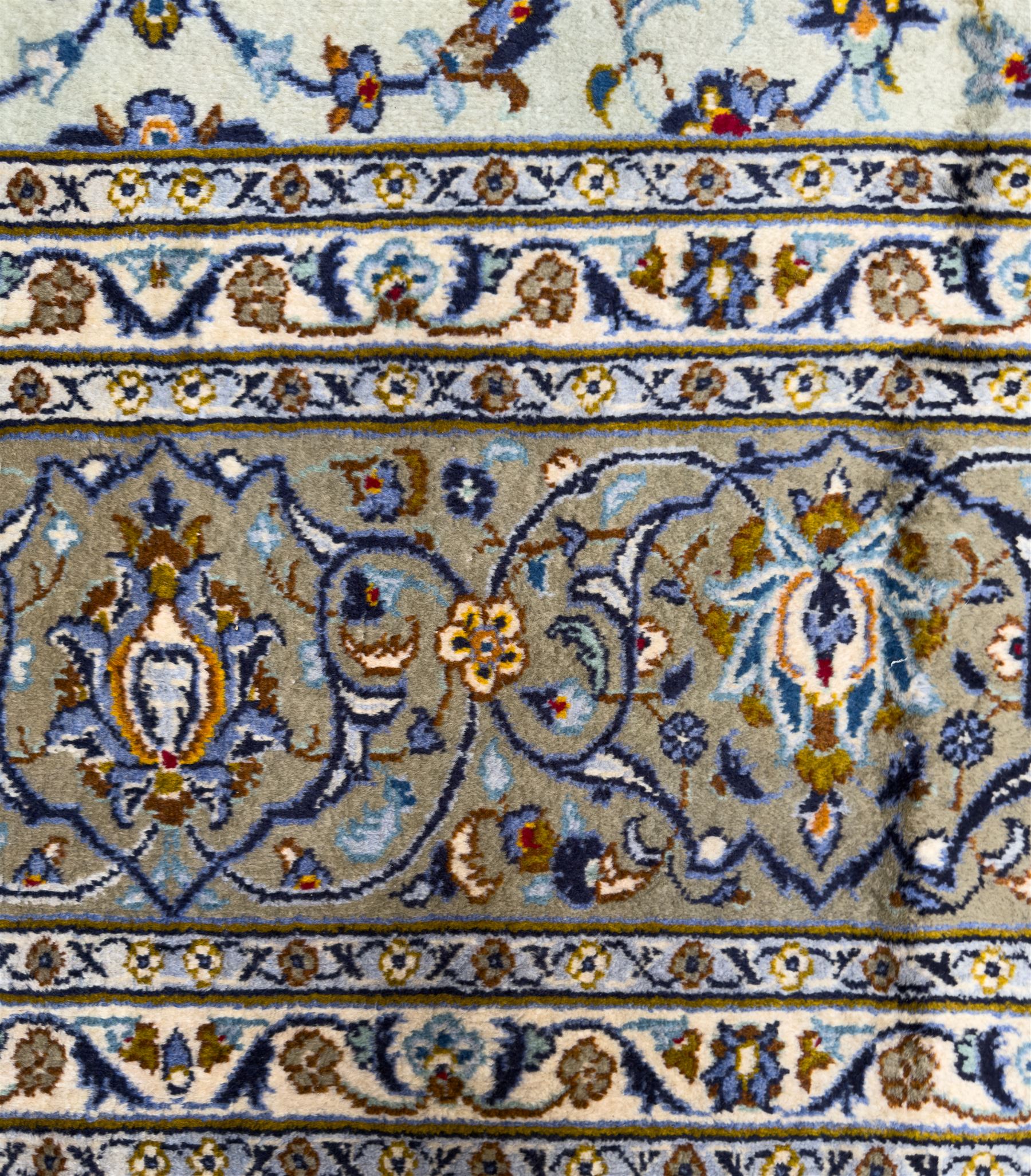 Central Persian Kashan hand-knotted carpet, the ivory ground intricately decorated with scrolling vines, palmettes, and stylised flowerheads in soft blue, gold and brown tones, enclosed by a broad indigo border with repeating floral motifs and multiple guard stripes