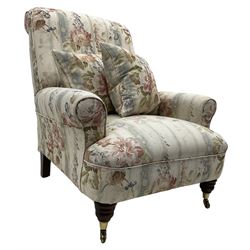 Victorian design armchair, rolled back and arms, upholstered in floral pattern fabric with two scatter cushions, on turned front feet with brass cups and castors