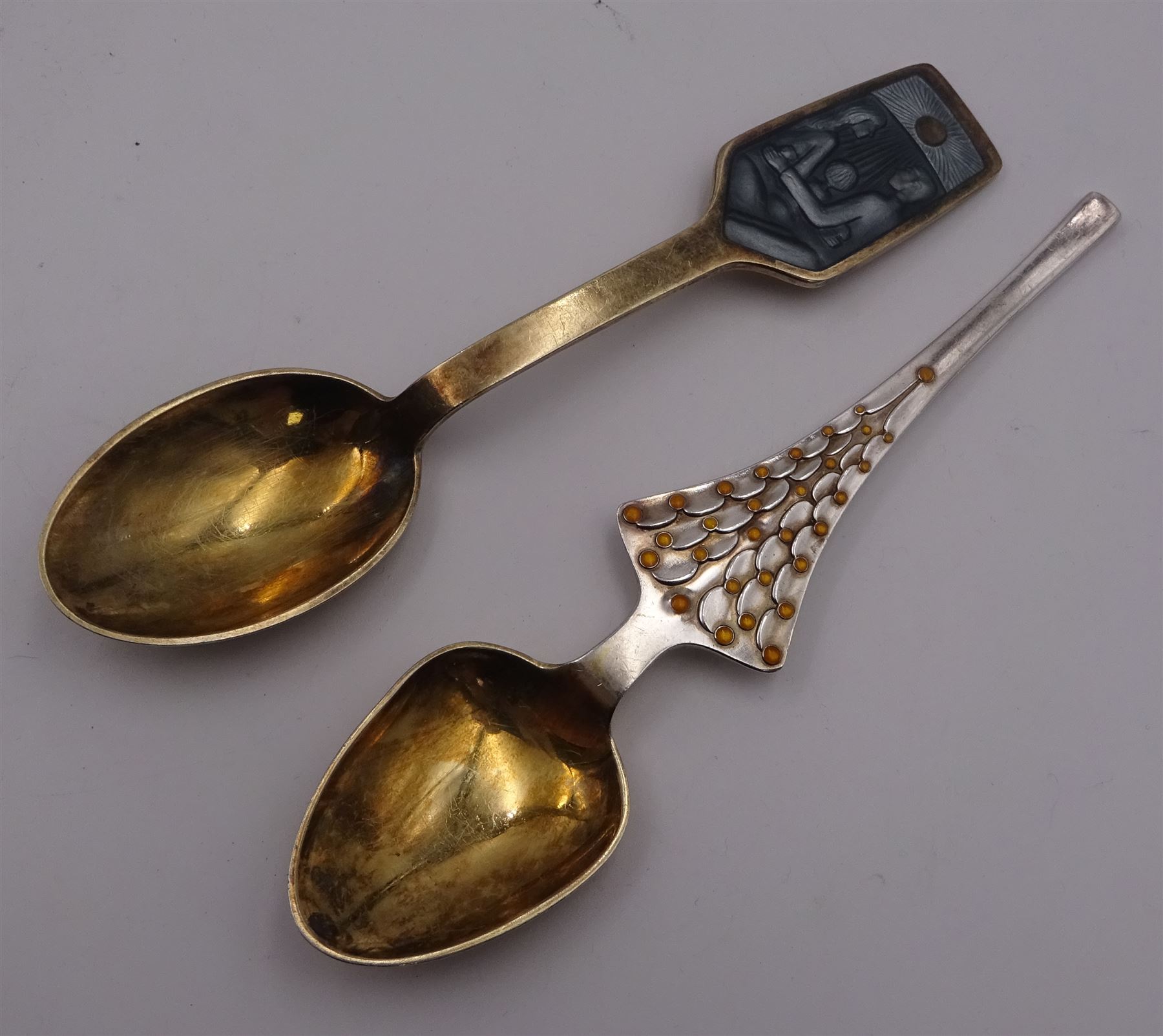 Two Danish silver-gilt year spoons by Georg Jensen, the first example decorated with enamel blue cornflower motif, dated 1972, in original pouch, the second example decorated with enamel pink briar rose motif, dated 1976, in original box, each impressed on underside RA AB, Sterling Denmark, and marked for Georg Jensen, together with two further examples by A.Michelson, the first with orange enamel fan design, dated 1965, impressed on underside A.Michelsen Sterling Danmark, TH, the second with enamel family scene, dated 1973, impressed on underside 925 S A.Michelsen Sterling Danmark, B Spang Olsen, approximate gross weight 6.11ozt (190.4 grams)