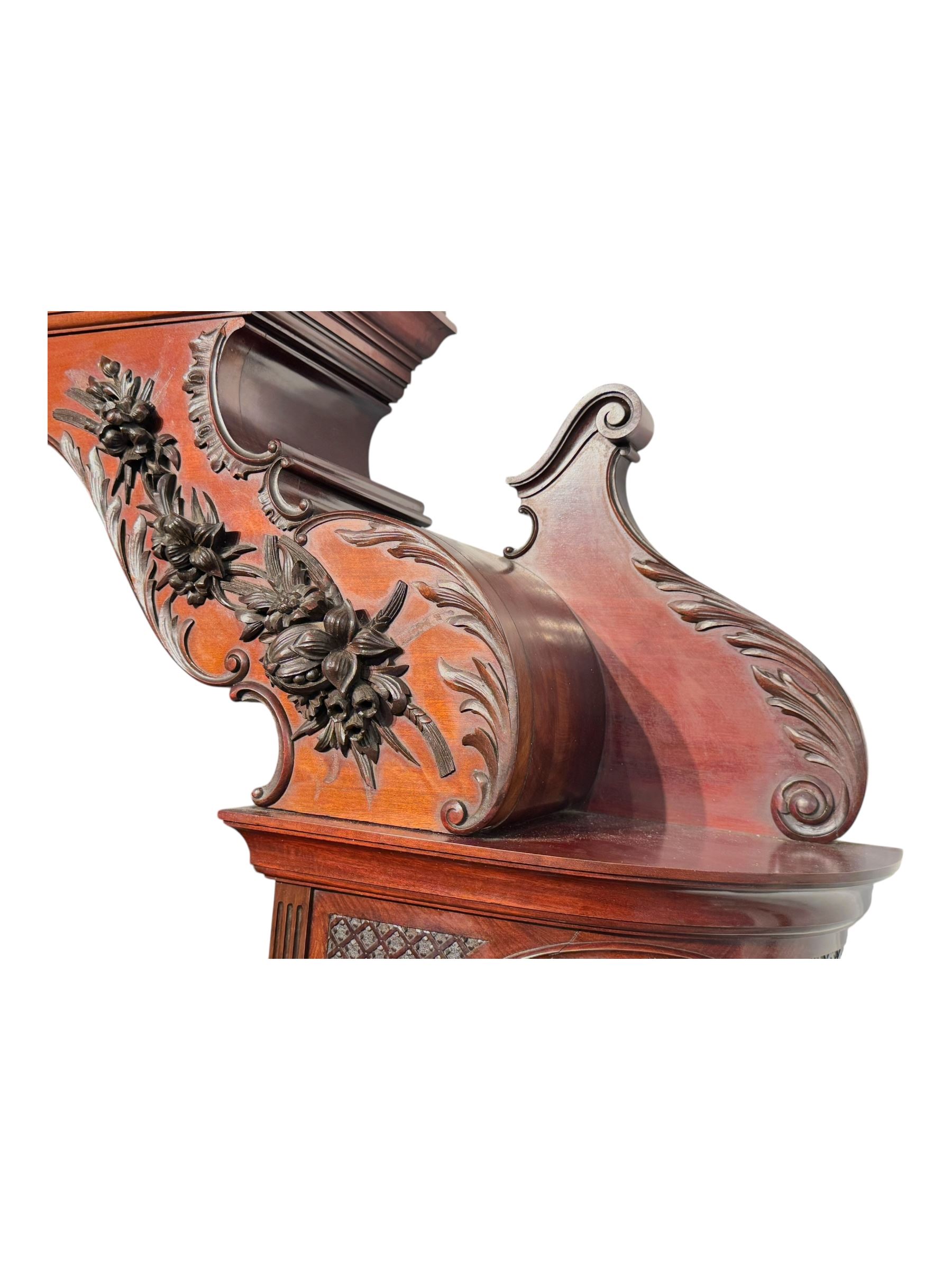 Late 19th century mahogany mirror back cabinet, shaped C-scroll pediment decorated with carved acanthus leaf cartouche and shells, shaped canopy top with applied foliate carvings over triple bevelled mirror back, central cupboard enclosed by panelled door carved with musical instruments, scrolls and shells, flanked by two glazed cabinets, on acanthus leaf carved cabriole supports united by undertier 