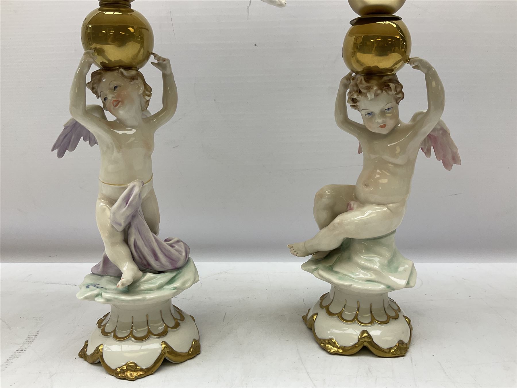 Pair of Capodimonte table lamps, in the form of cherubs holding a brass fitting, together with a pair of large Capodimonte figures in the form or a man and woman resting up on tree stump, largest example H57cm