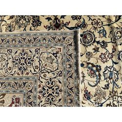 Persian Nain ivory ground carpet, central indigo medallion, the busy floral field decorated with scrolling vines and flower heads in shades of blue, beige, and red, wide guarded border with repeating palmettes and foliate motifs