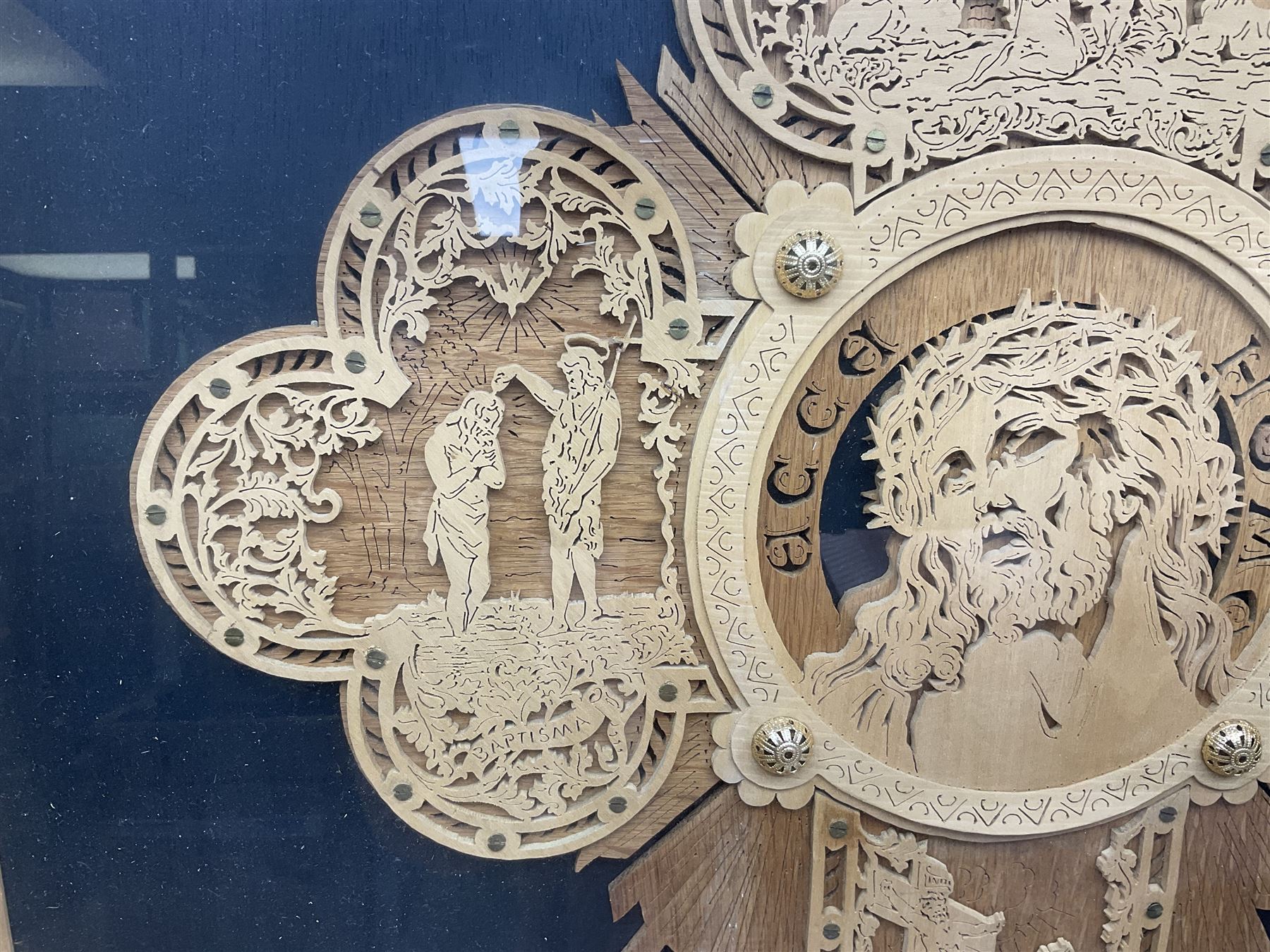 Cork carving of a religious cross depicting intricate scenes of various religious figures and motifs amongst trees and foliage, with central circular panel of Jesus Christ, in glazed frame, H95cm