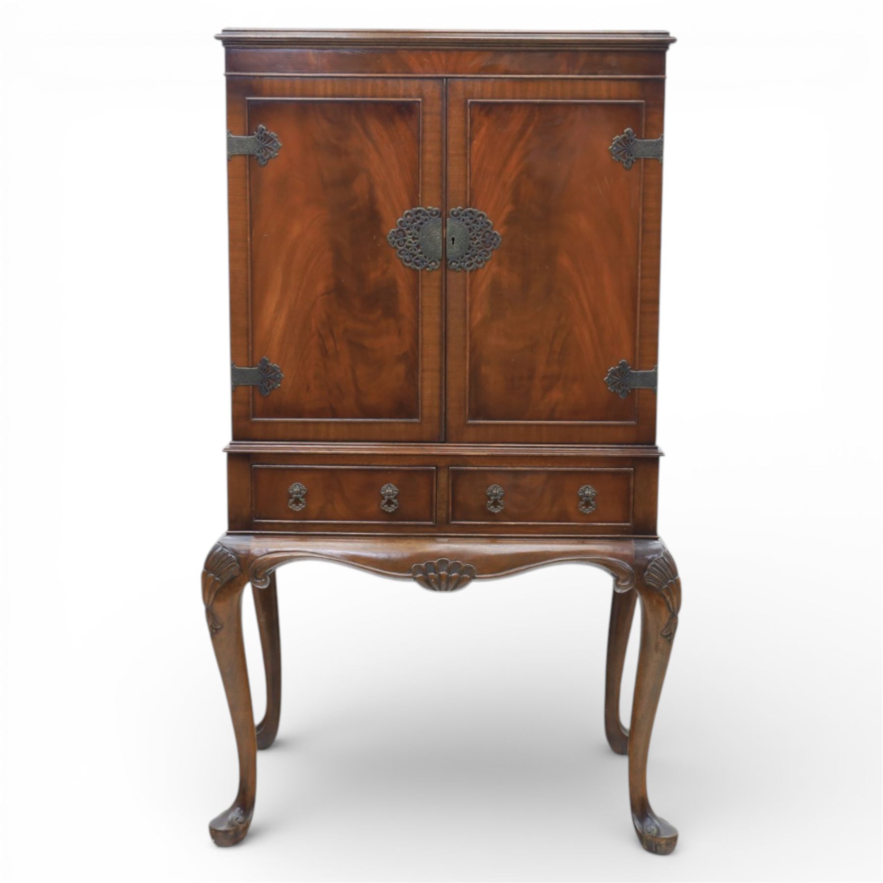 20th century Queen Anne style mahogany cocktail cabinet, moulded cornice above a pair of fielded panel doors with decorative strap hinges and central escutcheon, opening to a mirrored interior fitted with tiered shelves with brass gallery rails, pull-out glass inset mixing slide above three short drawers, shaped apron on cabriole supports with carved shell knees terminating in pad feet