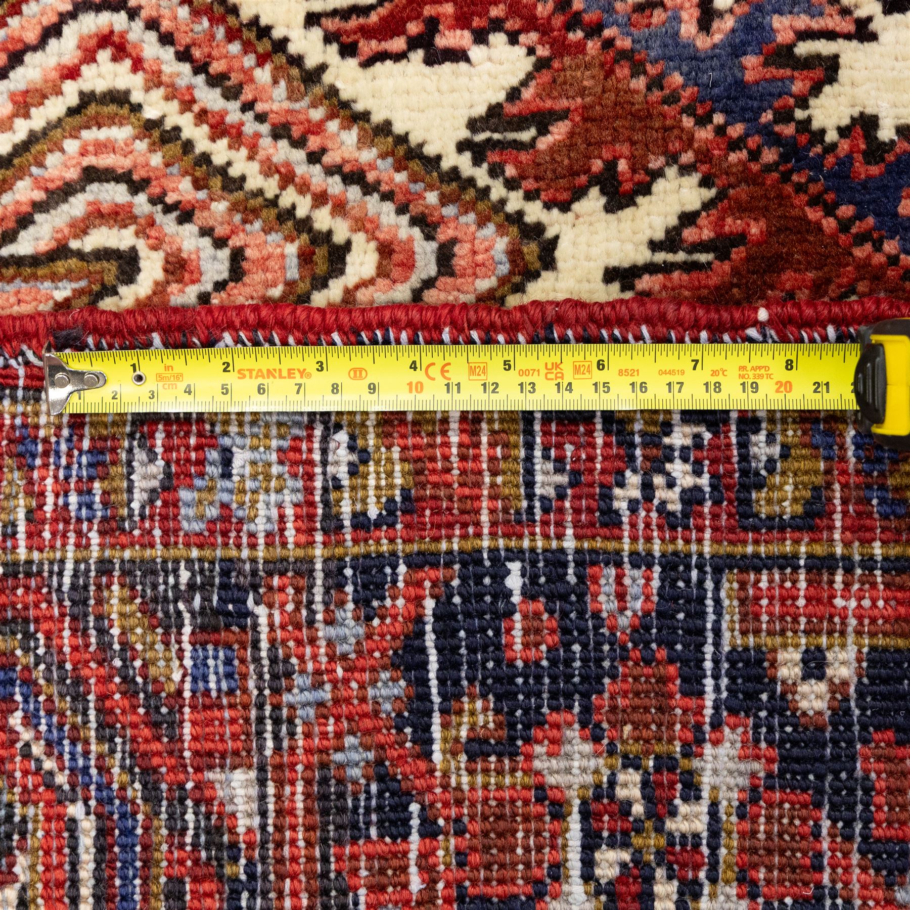 North West Persian Heriz hand-knotted carpet, madder red field, with a large angular stepped central medallion with serrated outlines, flanked by bold stylized palmettes, hooked leaves and geometric devices, spandrels similarly decorated within a wide geometric main border featuring angular floral motifs, enclosed by multiple guard borders in madder red, indigo blue, ivory, olive green and soft ochre, with cotton fringe ends 