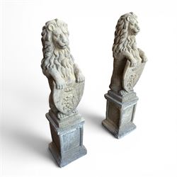 Pair of cast stone Heraldic lions, modelling in upright standing poses with flowing mane, each clasping an Armorial shield moulded with a crowned lion in their forepaws, raised on rectangular pedestals