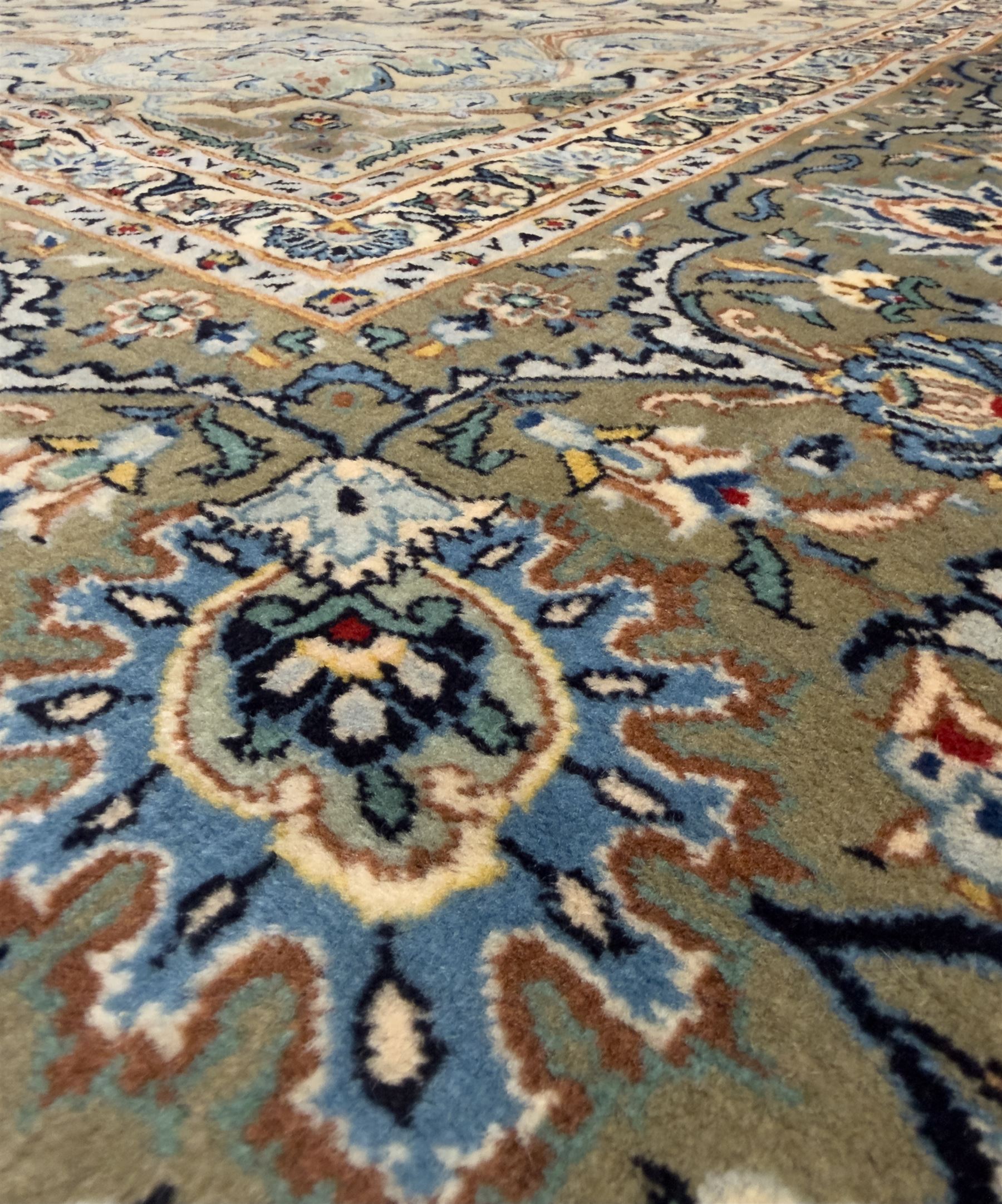 Central Persian Kashan hand-knotted carpet, ivory field with scrolling vines, palmettes, and rosettes around a cusped medallion with pendants and spandrels within a blue ground border of palmettes and flowerheads, 388cm x 300cm