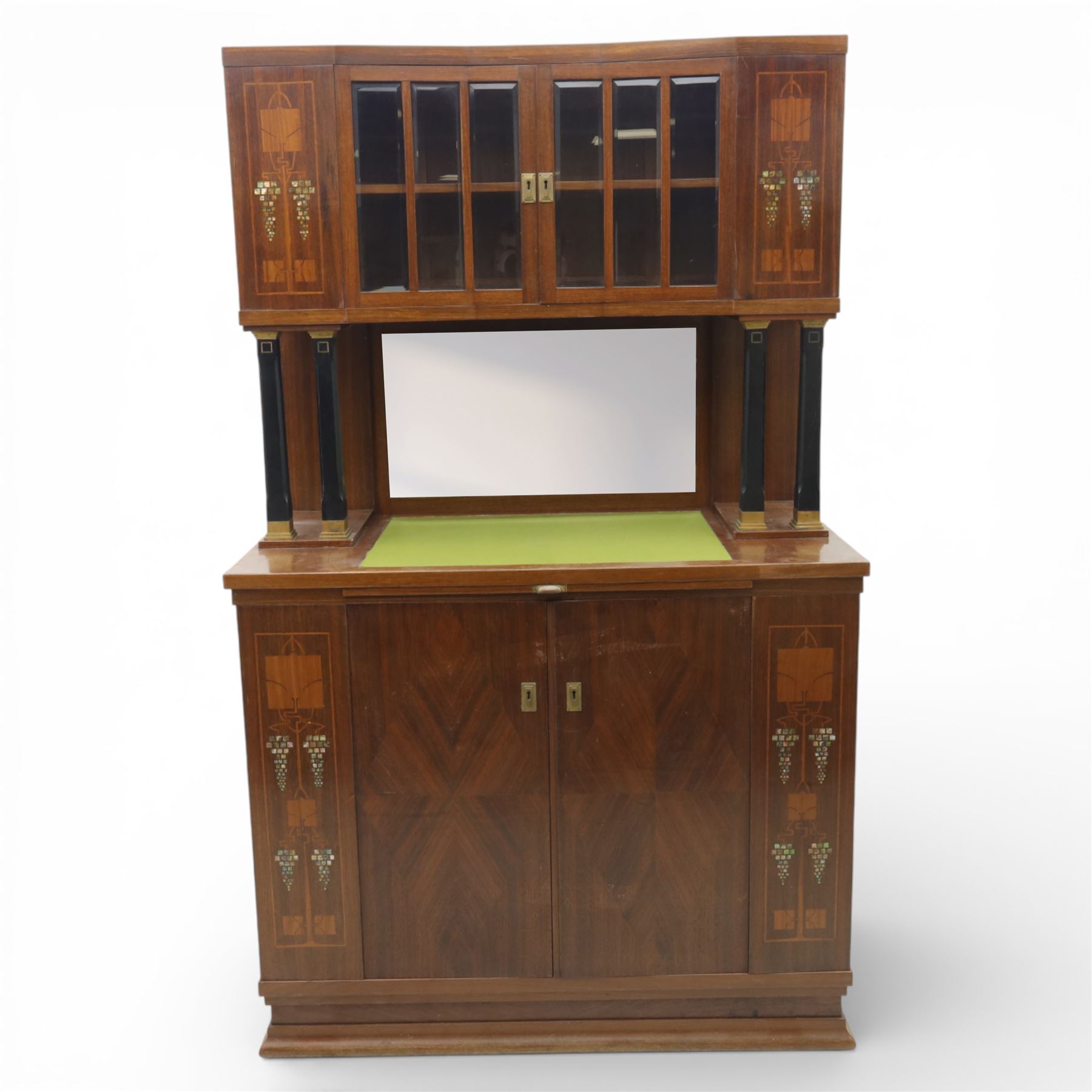 Continental Art Nouveau cocktail cabinet, the stepped cornice over a glazed upper section with panelled doors, enclosing fitted shelf, the central section with mirrored back and green baize serving surface flanked by ebonised and gilt detailed pilasters, the base fitted with cupboard doors inlaid with stylised foliate and geometric motifs, on a plinth base