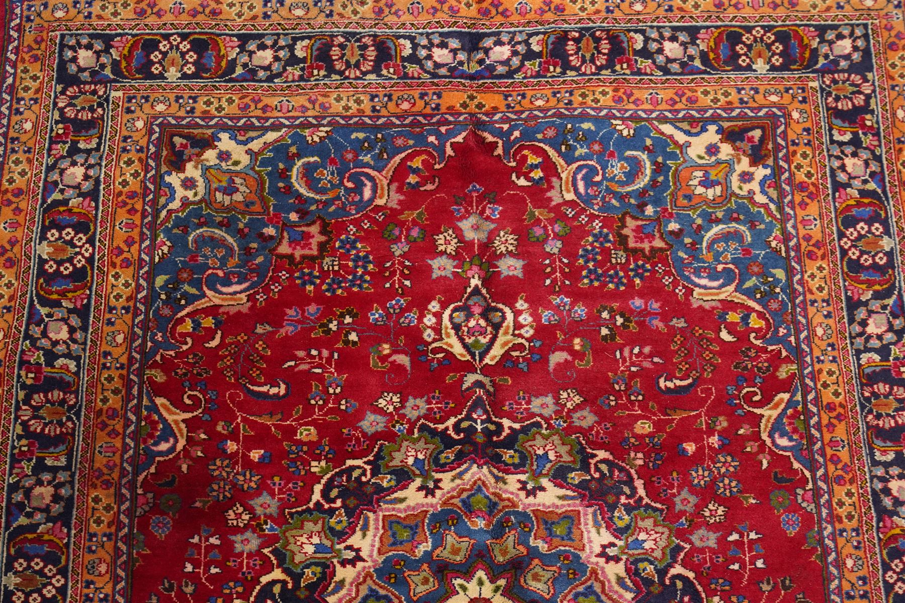 Persian Kashan hand-knotted rug, madder red ground centred by circular floral medallion with pendants, surrounded by scrolling vines, palmettes and flowerheads, dark navy spandrels, enclosed by dark navy floral border with multiple guard stripes