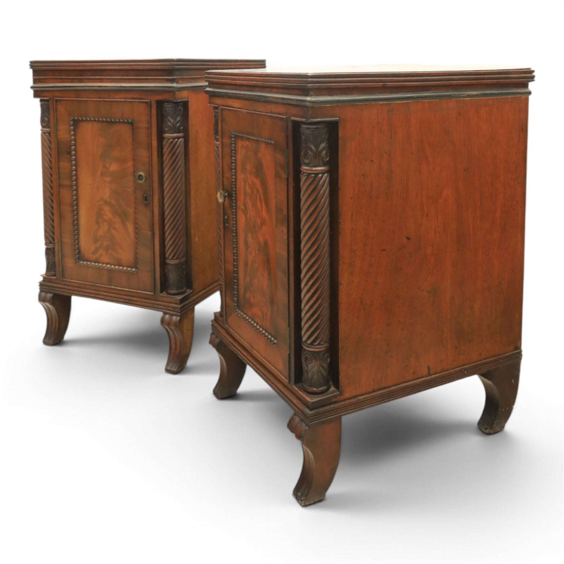  Pair of Regency mahogany bedside cabinets, rectangular top above a central cupboard door with flame mahogany veneer, flanked by spirally turned column uprights, raised on shaped supports