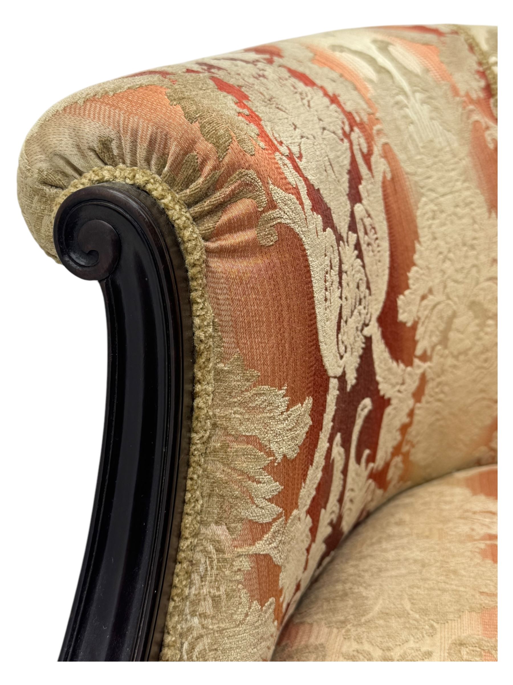 Early 20th century mahogany framed upholstered tub armchair, scrolled arms, upholstered in a damask-style fabric with foliate pattern, raised on cabriole front legs upon brass castors