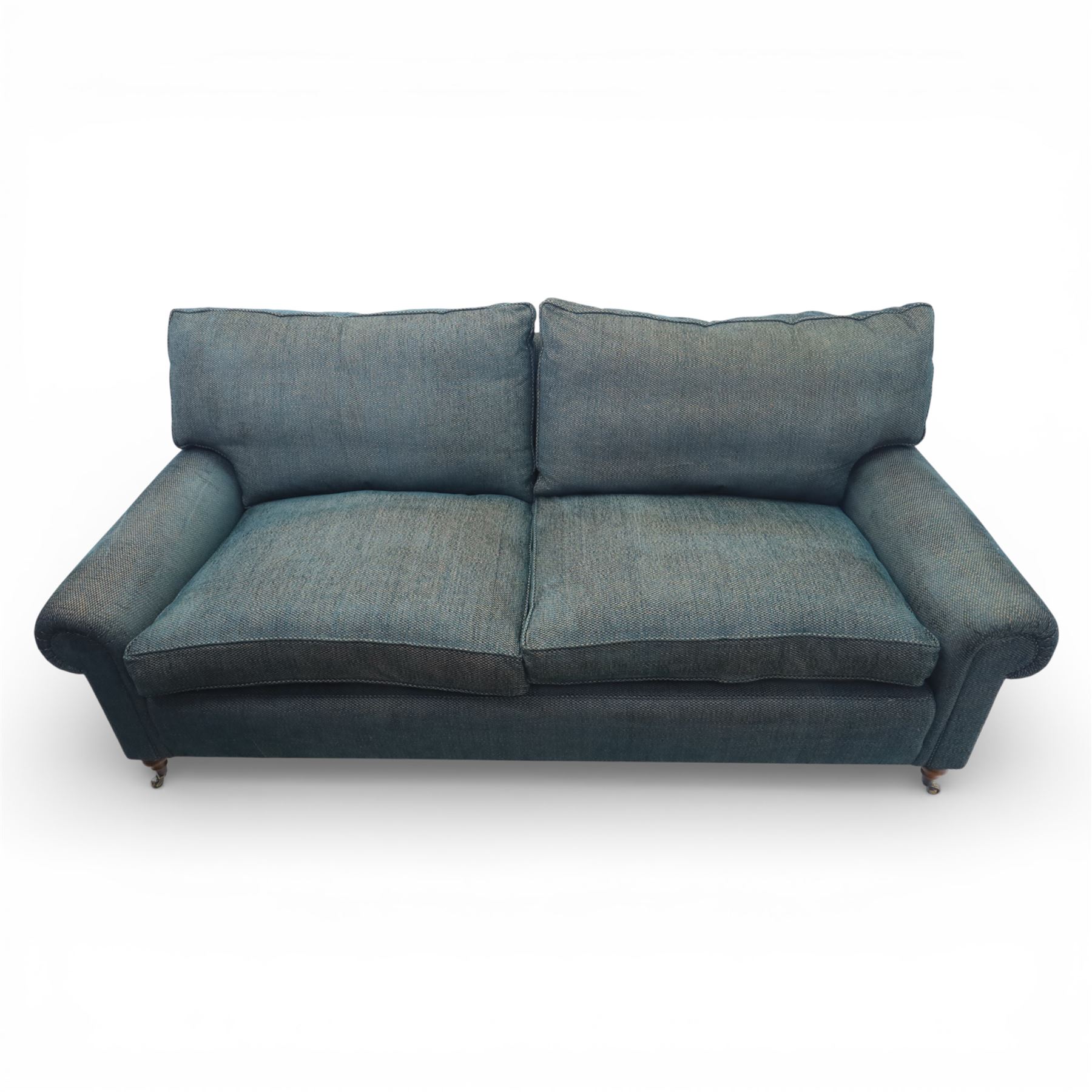 Late 20th century three seat sofa upholstered in green fabric, with gently rounded scroll arms, loose seat and back cushions, raised on turned wooden legs with castors, rear splayed legs