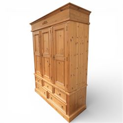 20th century pine wardrobe with drawer base, moulded cornice over three fielded panel cupboard doors enclosing hanging compartments, the base fitted with three short and two long drawers with brass ring handles, raised on a plinth base