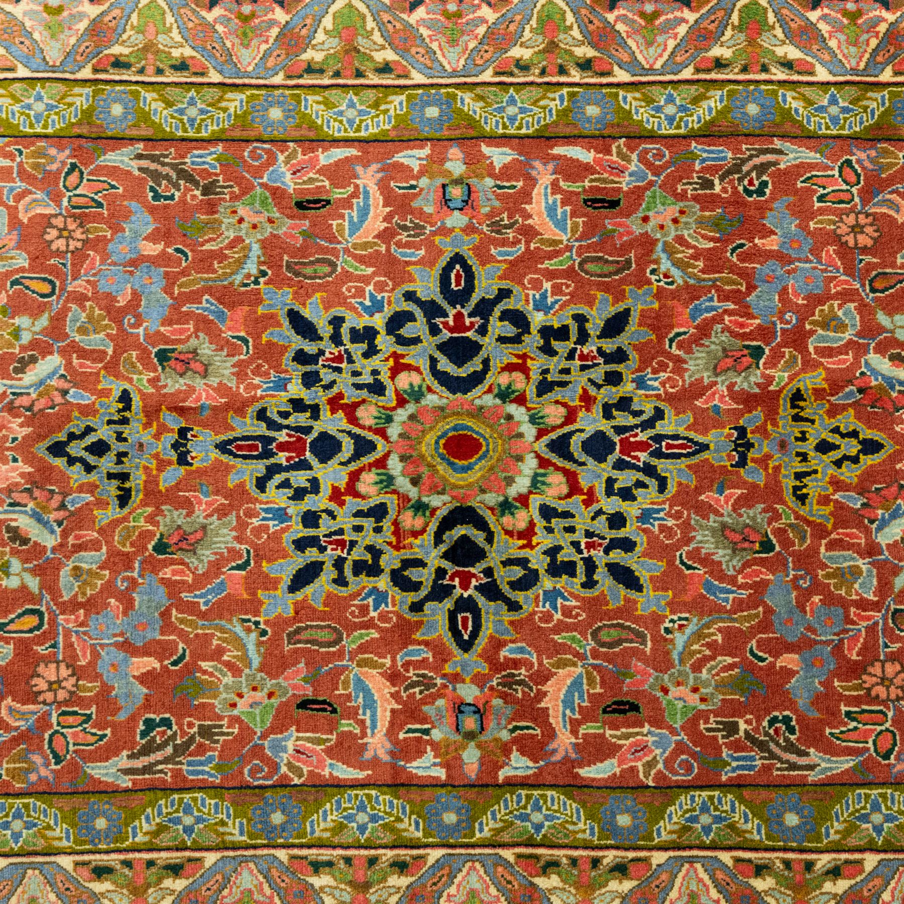 South Persian Sirjan hand-knotted carpet, terracotta ground, with a central shaped dark navy floral medallion with pendants, surrounded by scrolling foliate and floral motifs incorporating palmettes, rosettes and stylised vine work in blue, green and ivory tones, enclosed by dark navy spandrels and a wide green and ivory border with repeating palmettes and angular leaf motifs, flanked by patterned guard stripes, with cotton fringes