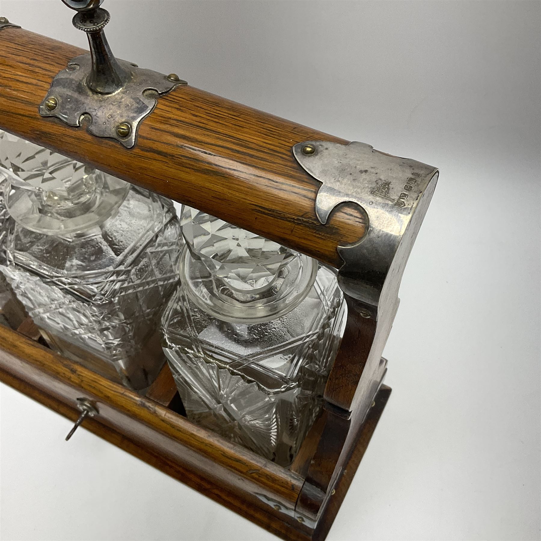 A Mappin & Webb silver plate mounted oak tantalus, containing three square sided cut glass decanters, complete with key, H35cm, together with a further square sided decanter. 