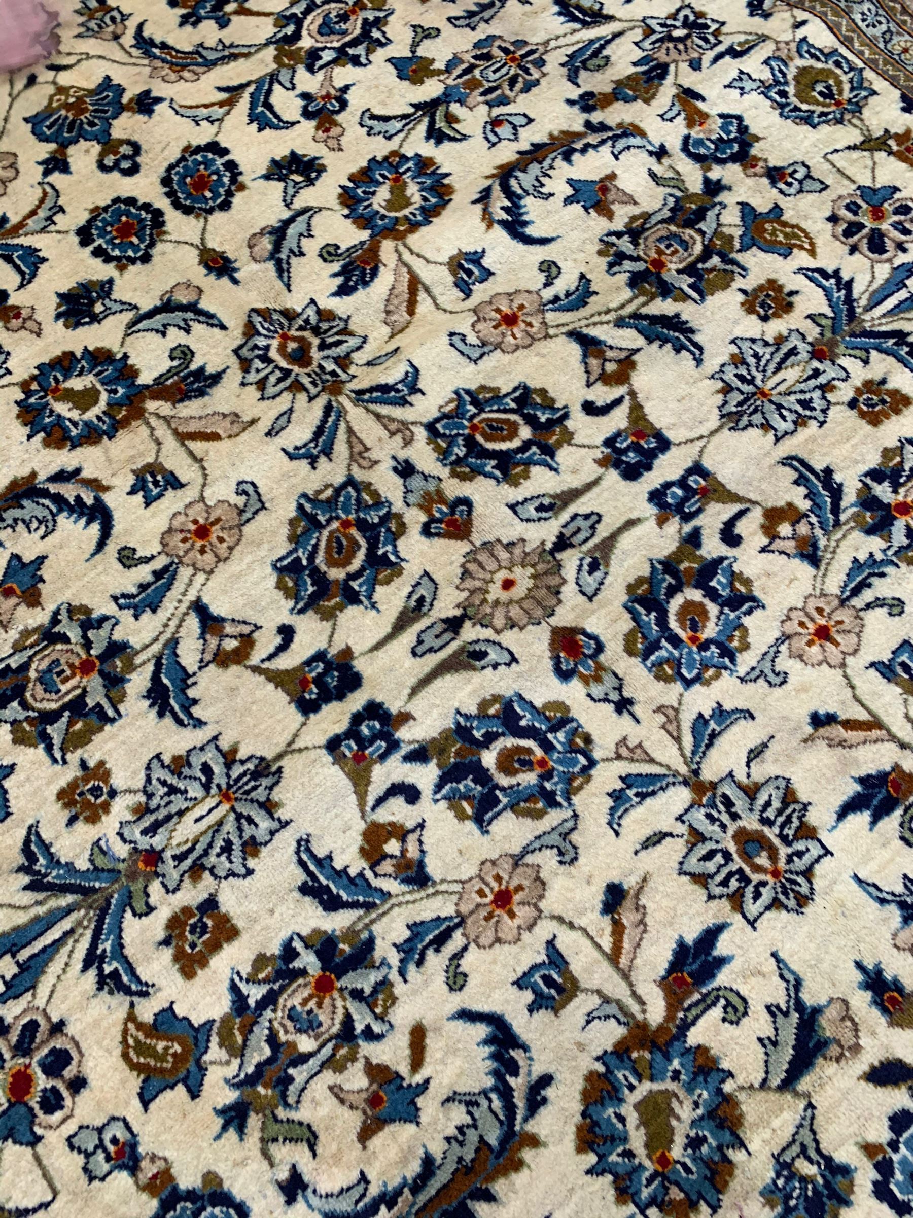 Persian Kashan ivory ground rug, the field decorated with stylised plant motifs and interlacing leafy branches, scrolling border decorated with further plant motifs, floral design guard bands  