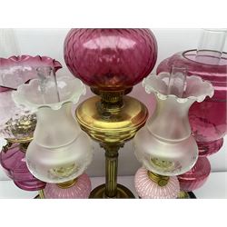 Victorian cast brass oil lamp, with fluted pink glass shade, together with two smaller brass oil lamps with pink shades and reservoirs and a pair of oil lamps, the bases modelled as putti, with pink glass reservoir  and frosted shades, tallest H70cm